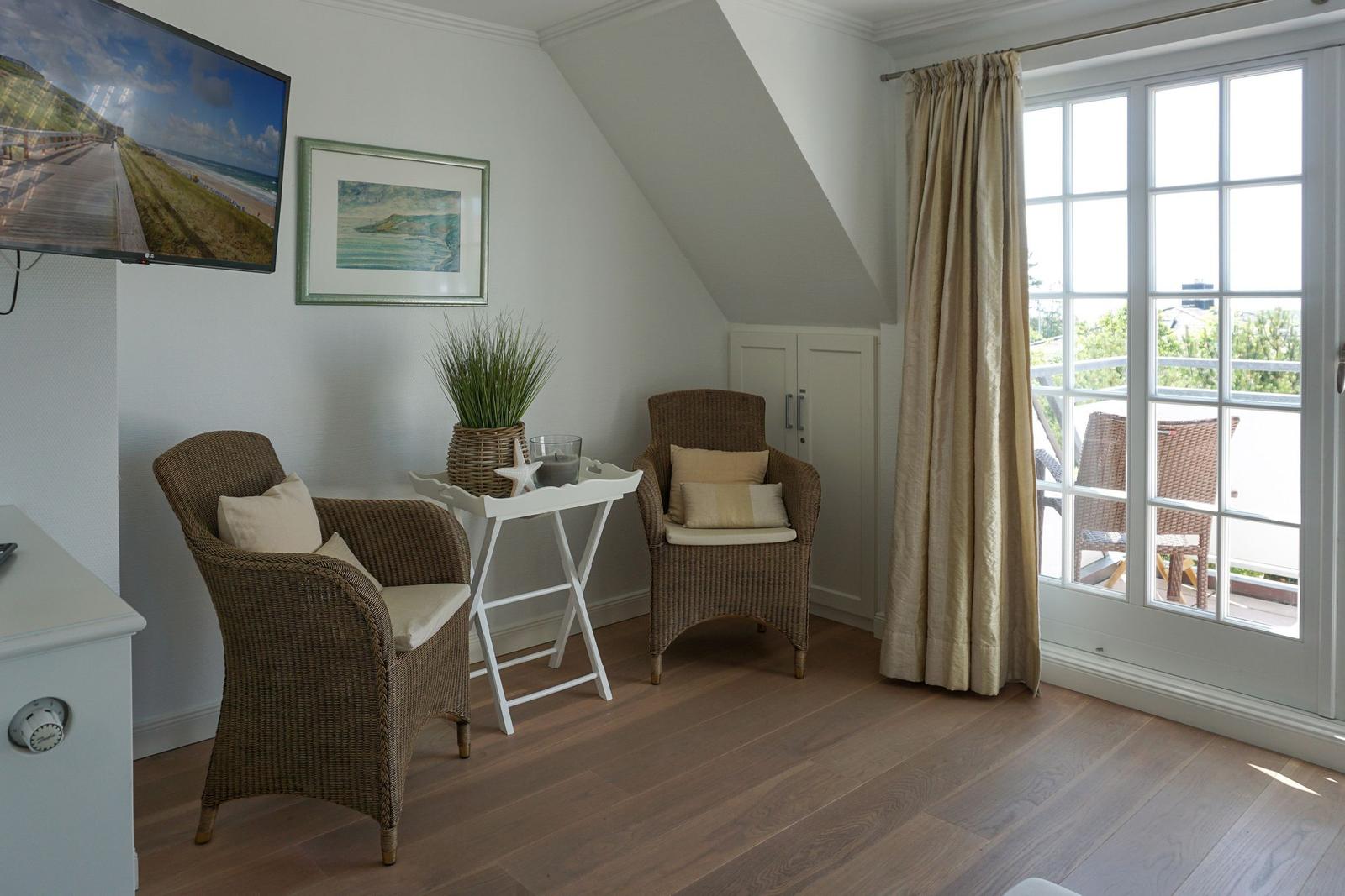 Zimmer mit zwei Rattan-Stühlen, Fernseher und Balkontür mit Blick.