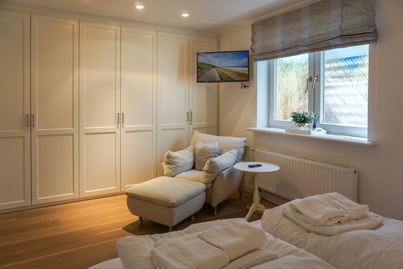 Schlafzimmer mit Bett, Sessel, TV und Fenster mit Blick auf Strand.