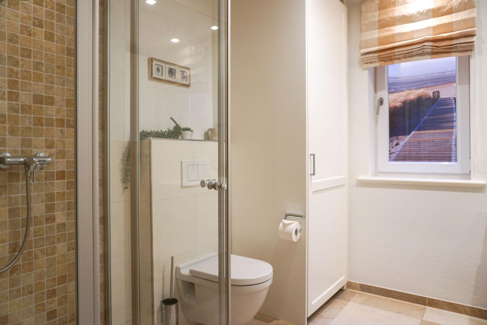 Bad mit Dusche, Toilette und Fenster mit Strandbild.