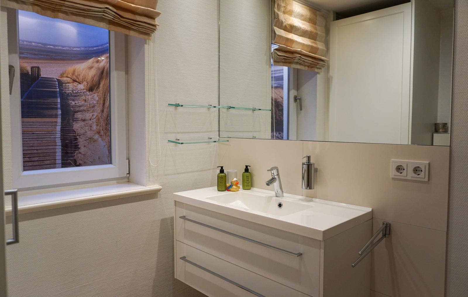 Badezimmer mit Waschbecken, Spiegel und Fenster mit Strandbild
