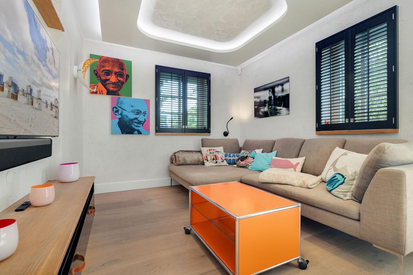 Wohnzimmer mit Sofa, orangefarbenem Couchtisch und Wandbildern.