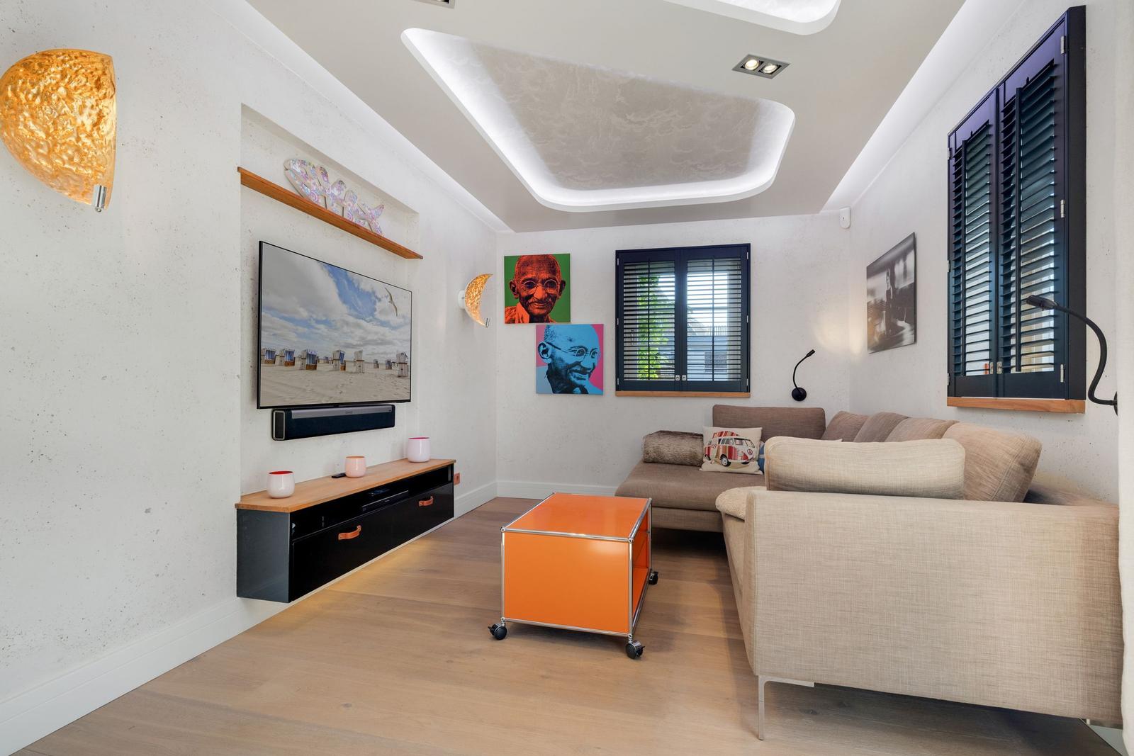 Wohnzimmer mit Sofa, Fernseher und orangefarbenem Tisch.