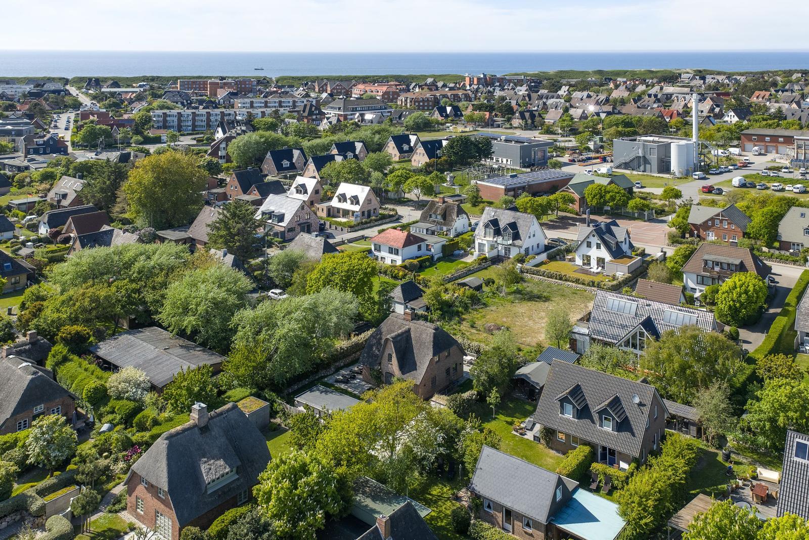 Aerial view of a coastal town with houses, greenery, and the sea in the background.
