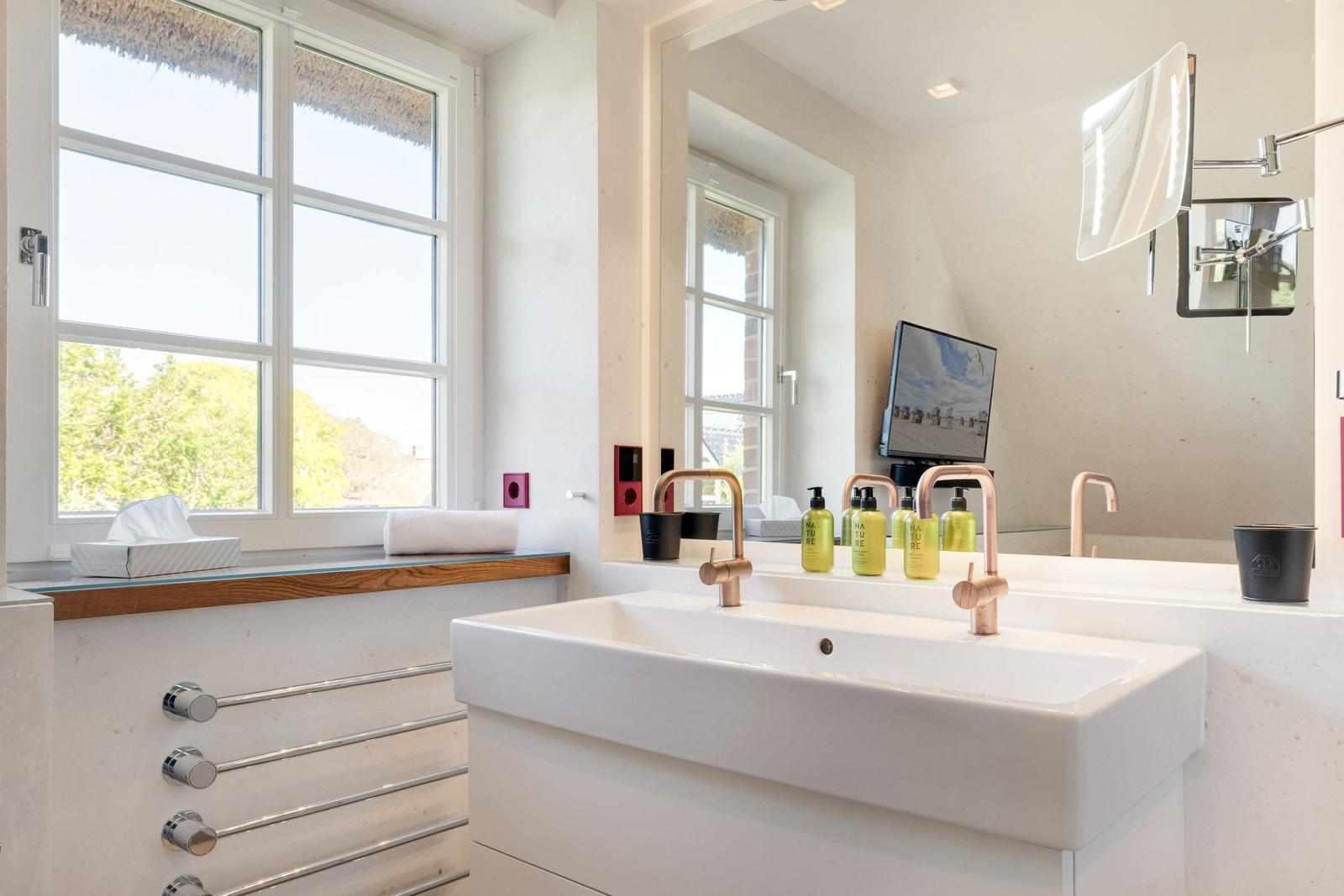 Badezimmer mit Waschbecken, Spiegel und Fenster mit Blick auf Grün.