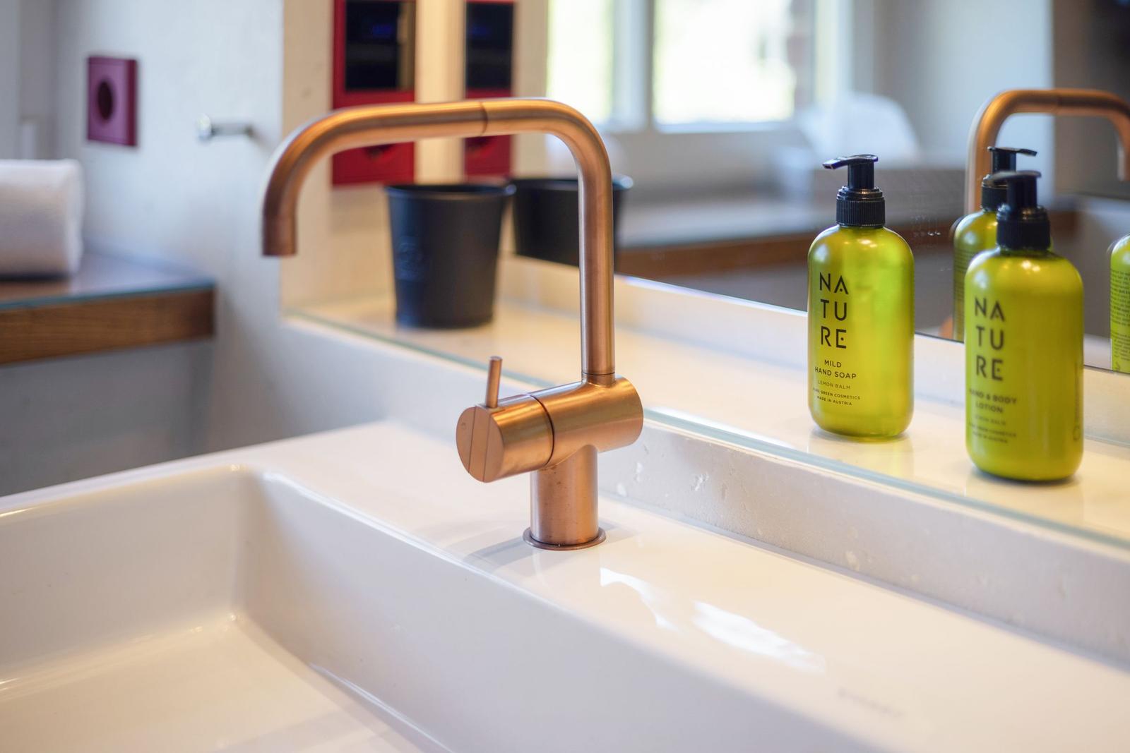 Waschbecken mit Kupferhahn und grünen Pflegeprodukten