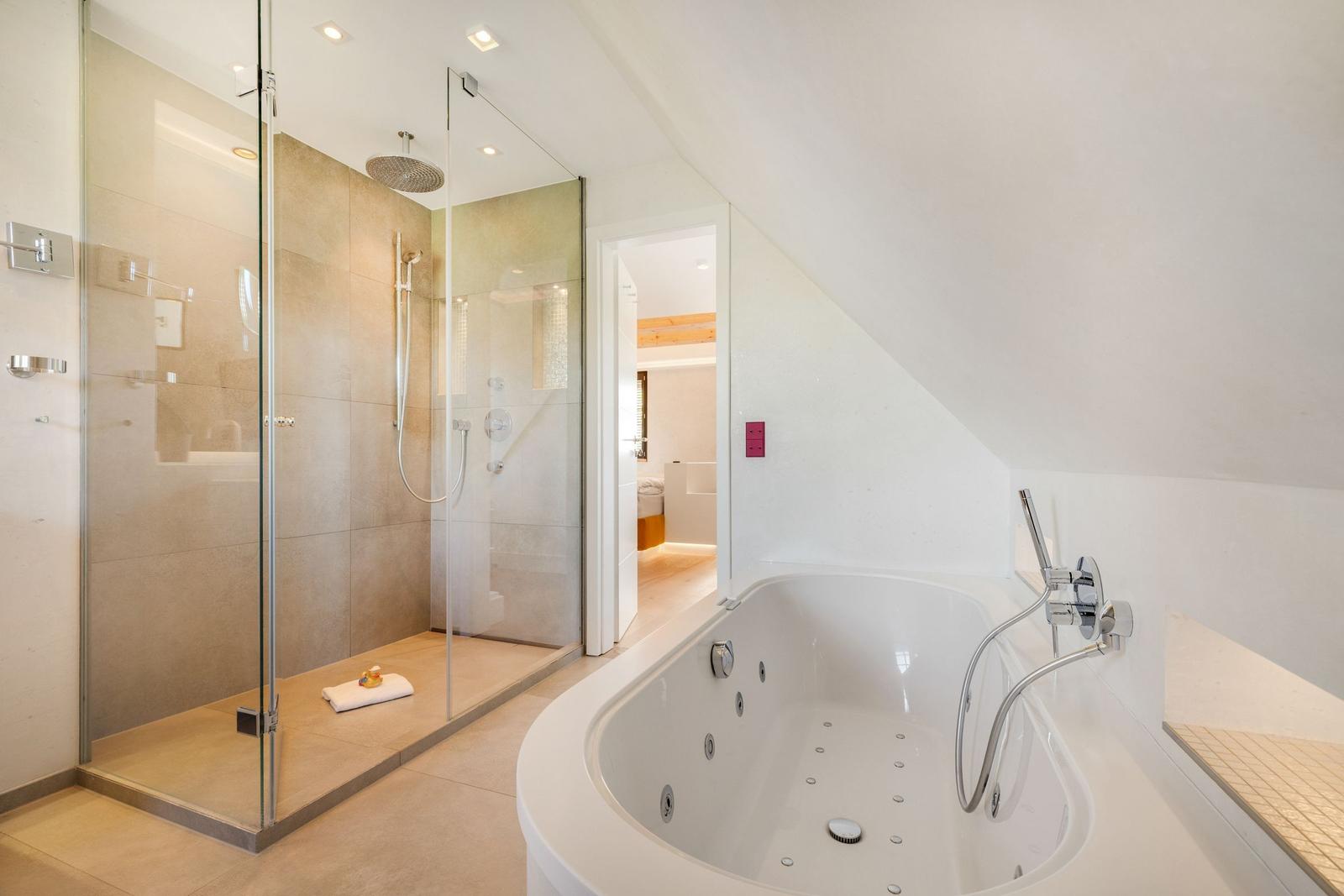Dusche mit Glaswand und Badewanne mit Massagefunktion.
