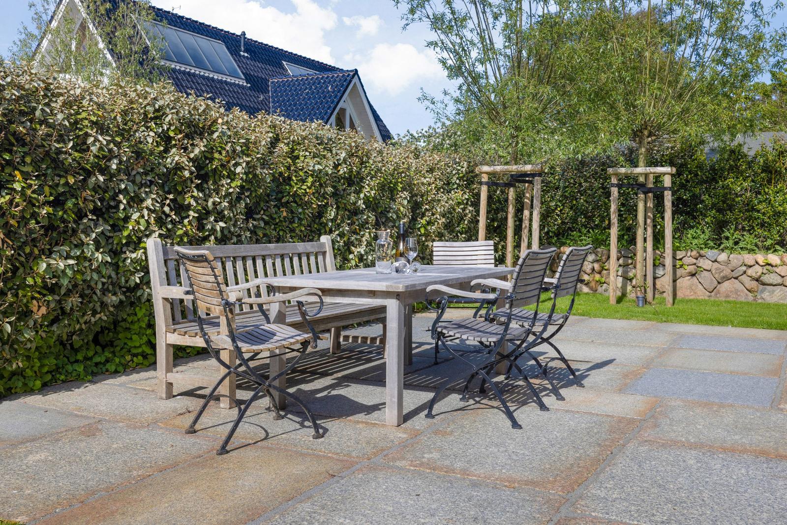 Terrasse mit Tisch und Stühlen, umgeben von Hecke und Grünflächen.