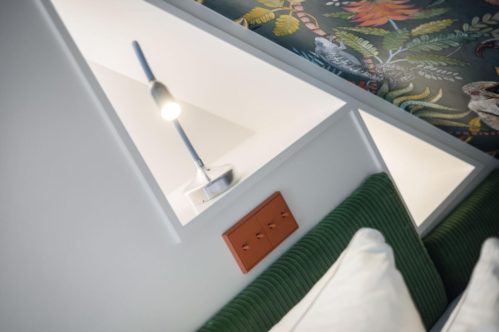 Bettkopfteil mit grünem Stoff, Lampe und Wandbehang mit Tiermotiven.