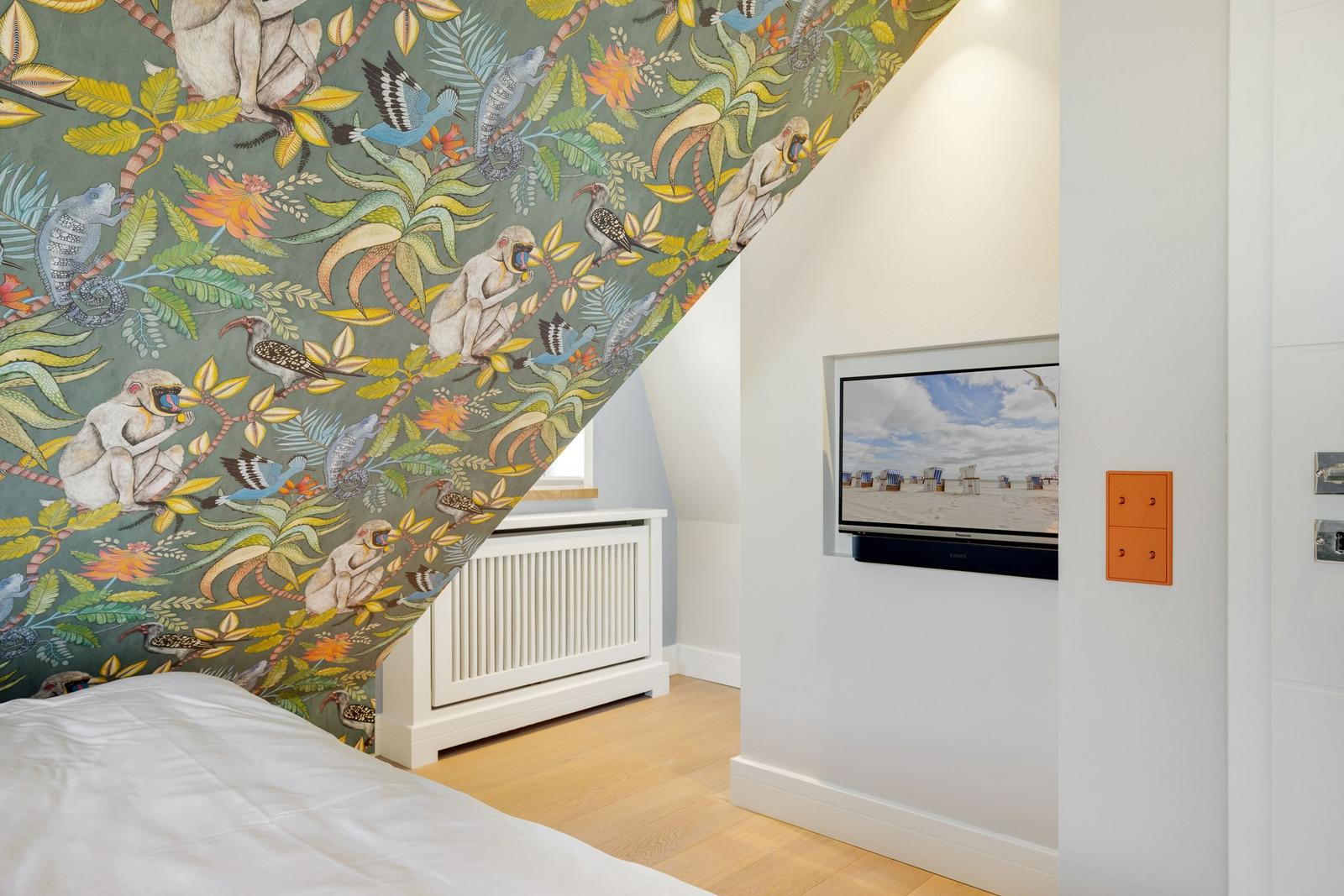 Schlafzimmer mit Tiermotiv-Wandtapete, Fernseher und weißem Heizkörper.