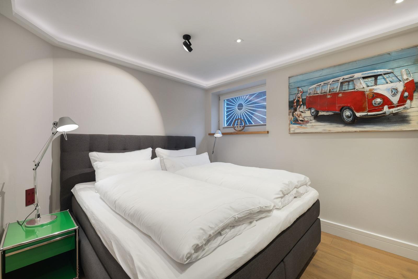 Schlafzimmer mit Doppelbett, grünem Nachttisch und Wandbild eines VW-Busses.