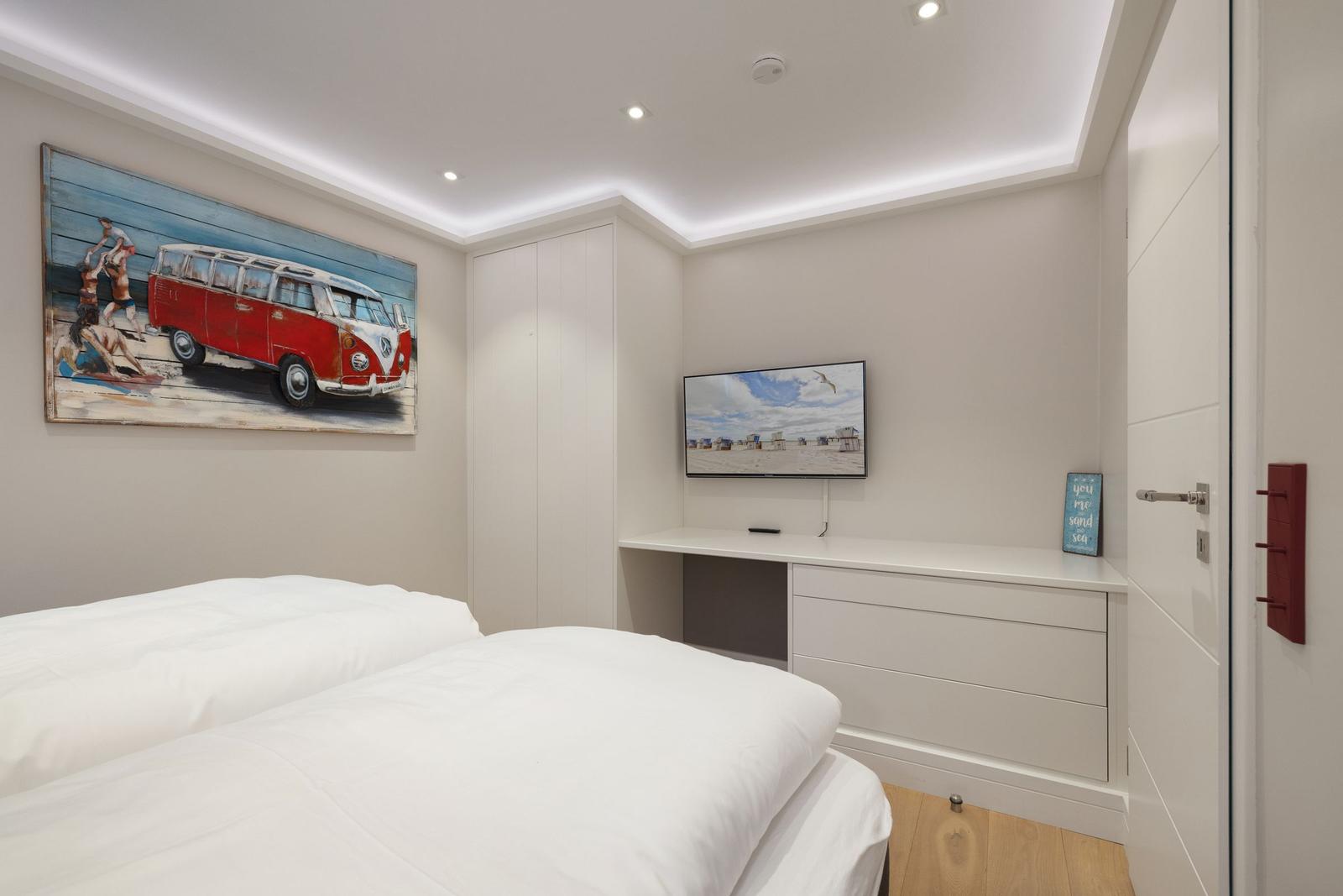 Schlafzimmer mit Bett, Fernseher und Wandbild. Holzboden und weiße Möbel.