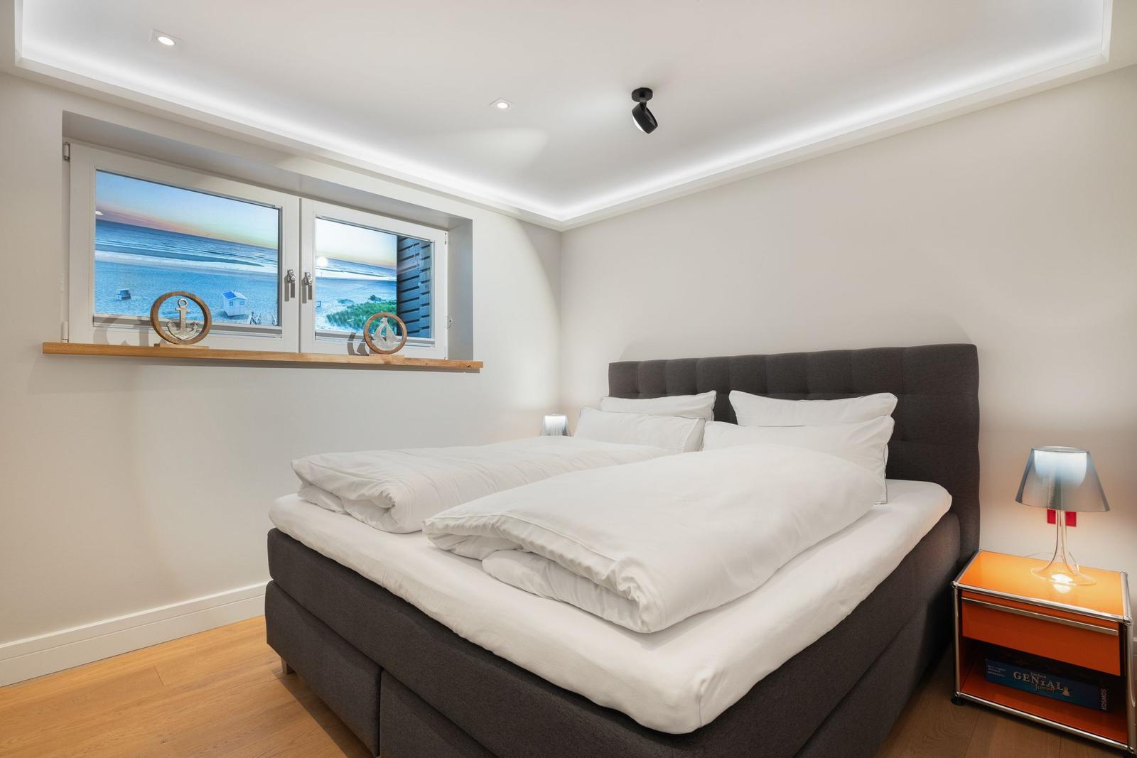 Schlafzimmer mit Bett, Nachttisch und Fenster mit Meerblick.