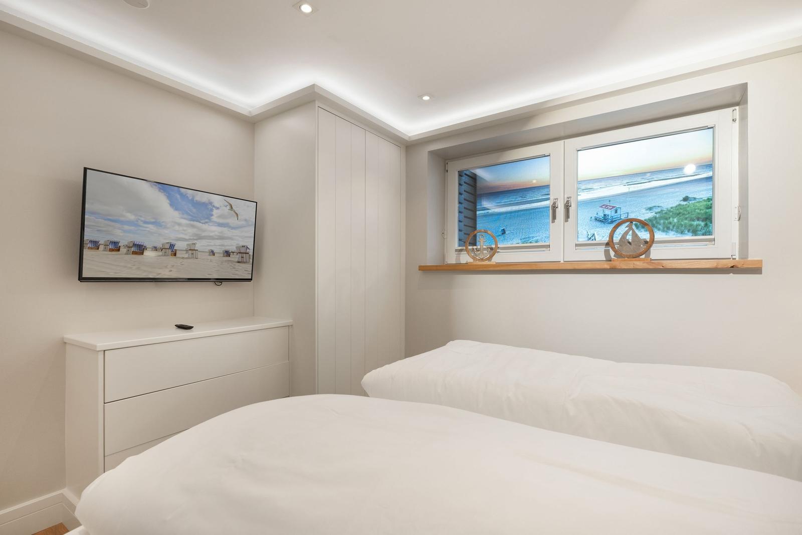 Zwei Betten, TV und Fenster mit Meerblick in einem Schlafzimmer.