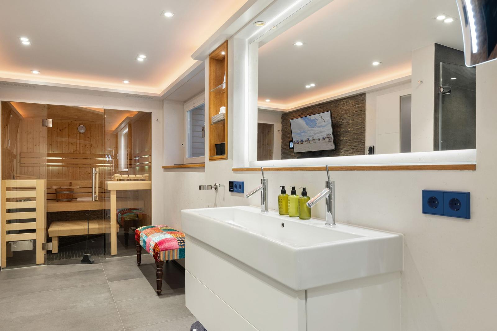 Bad mit Dusche, Waschbecken und Sauna im Hintergrund.