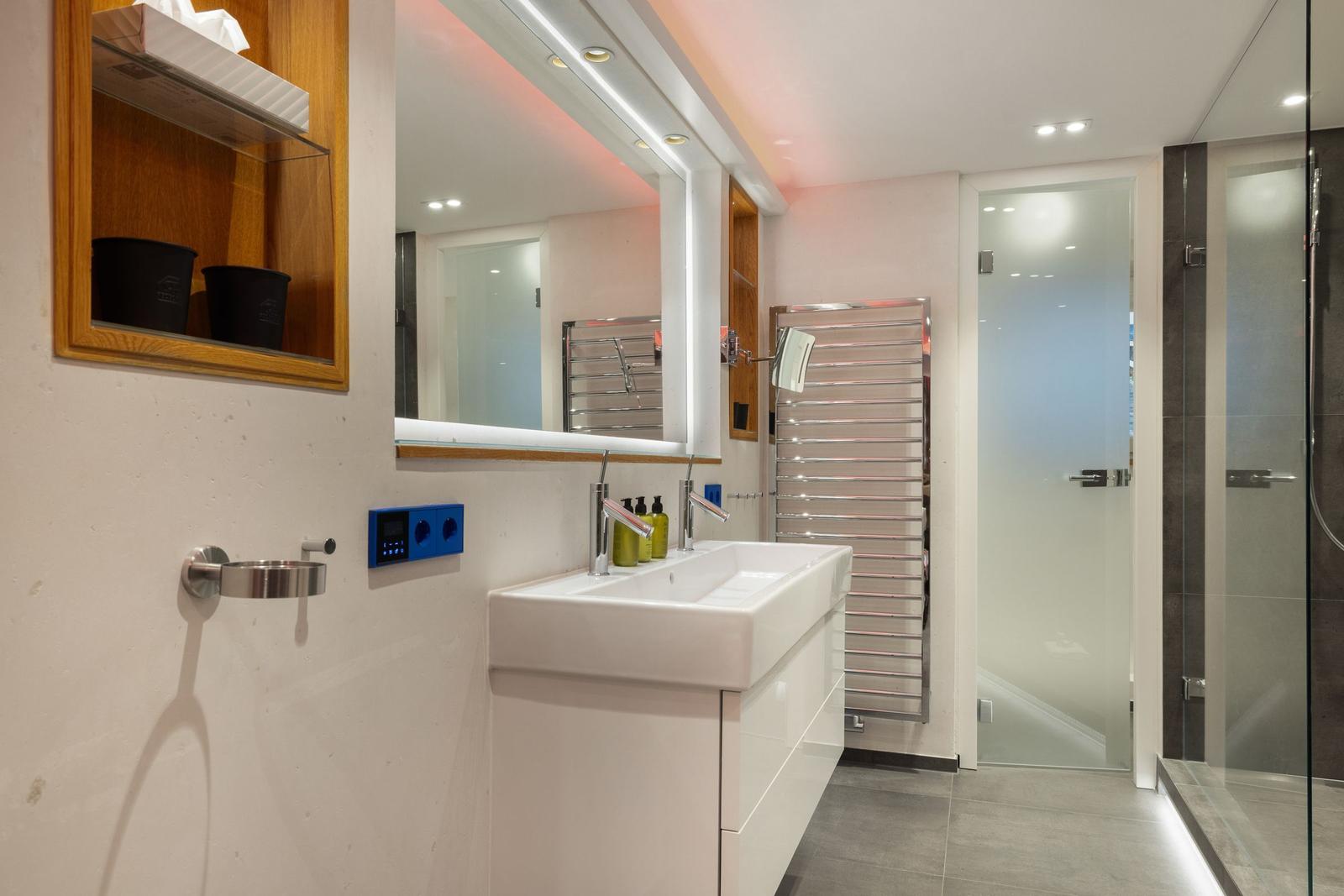Badezimmer mit Waschbecken, Spiegel, Dusche und Heizkörper.