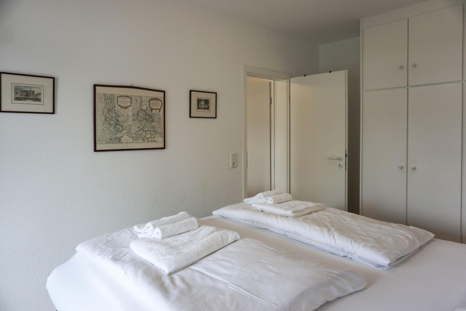 Zwei Betten mit weißen Bettwäsche und Handtüchern. Wand mit drei Bildern und Kleiderschrank.