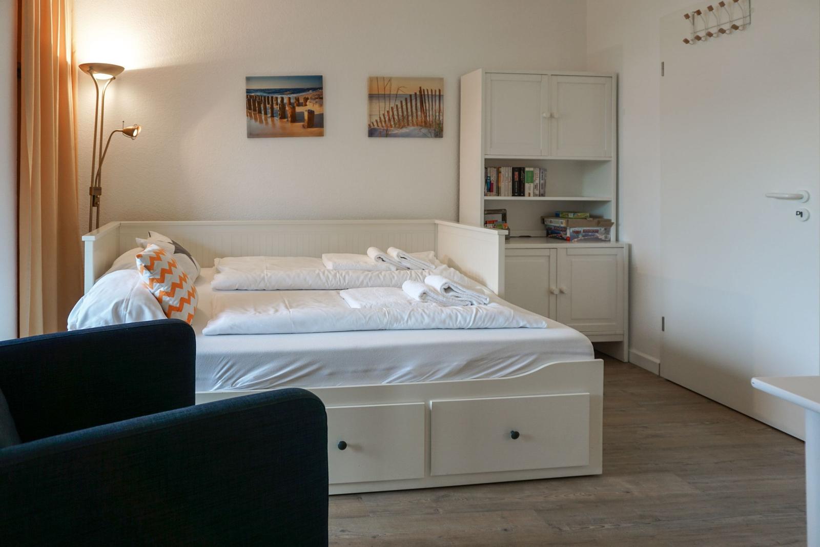 Schlafzimmer mit weißem Bett, Nachttisch, Wandbildern und Stauraum.