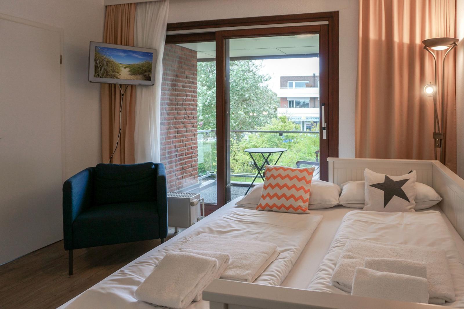 Schlafzimmer mit Balkon, Bett, Sessel und Fernseher.