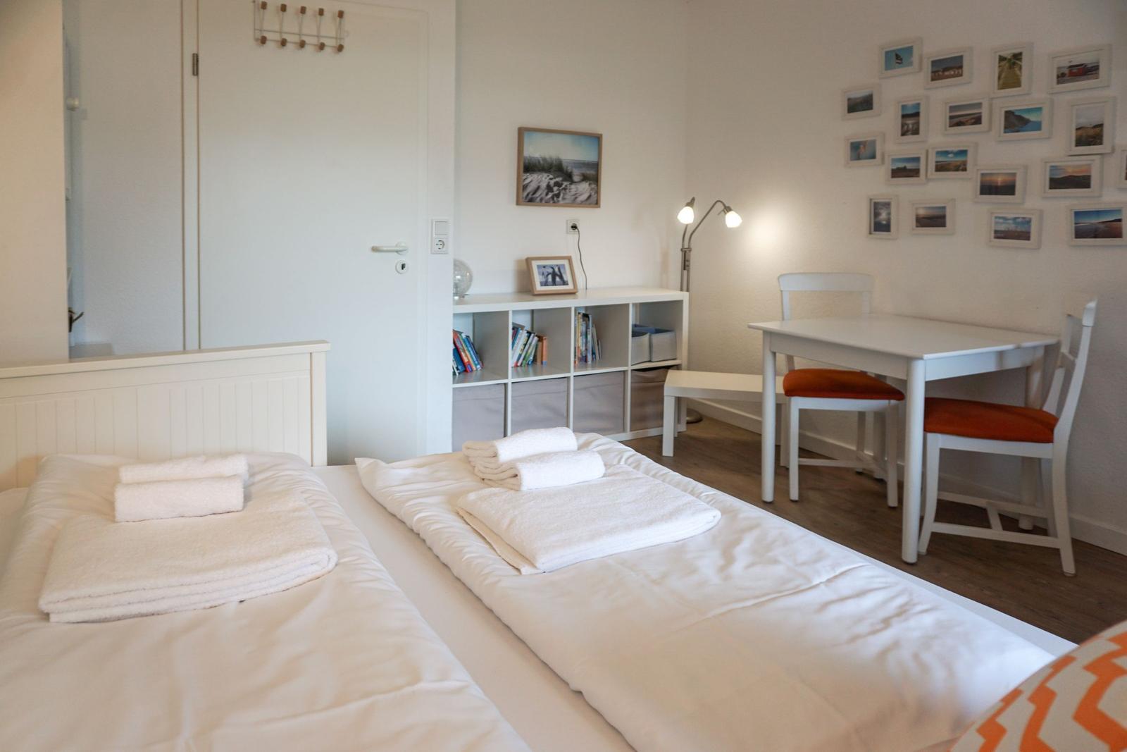 Zwei Betten mit weißen Laken und Handtüchern. Tisch mit Stühlen und Wandbilder.