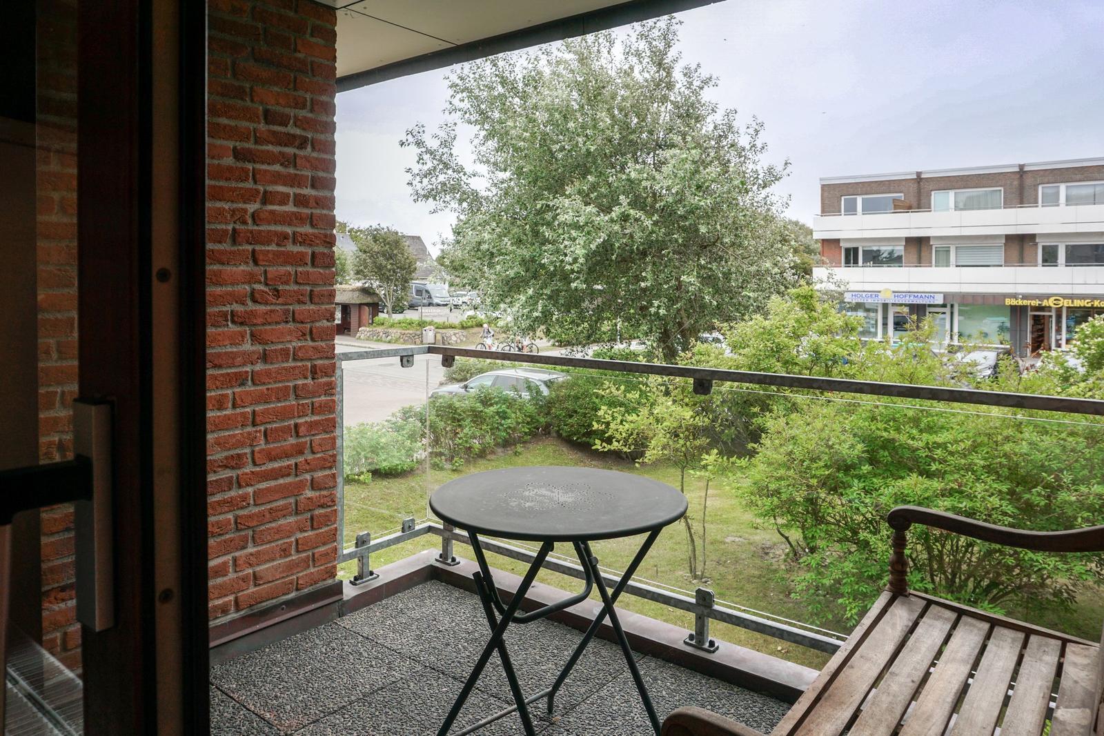 Terrasse mit Tisch und Bank. Blick auf Grünflächen und Gebäude.