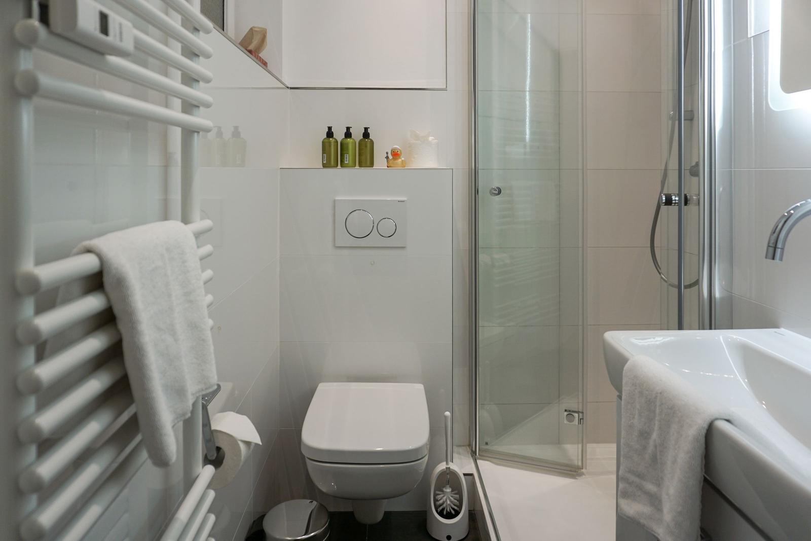 Badezimmer mit Dusche, Toilette und Waschbecken. Handtuchhalter und Duschdusche sind vorhanden.