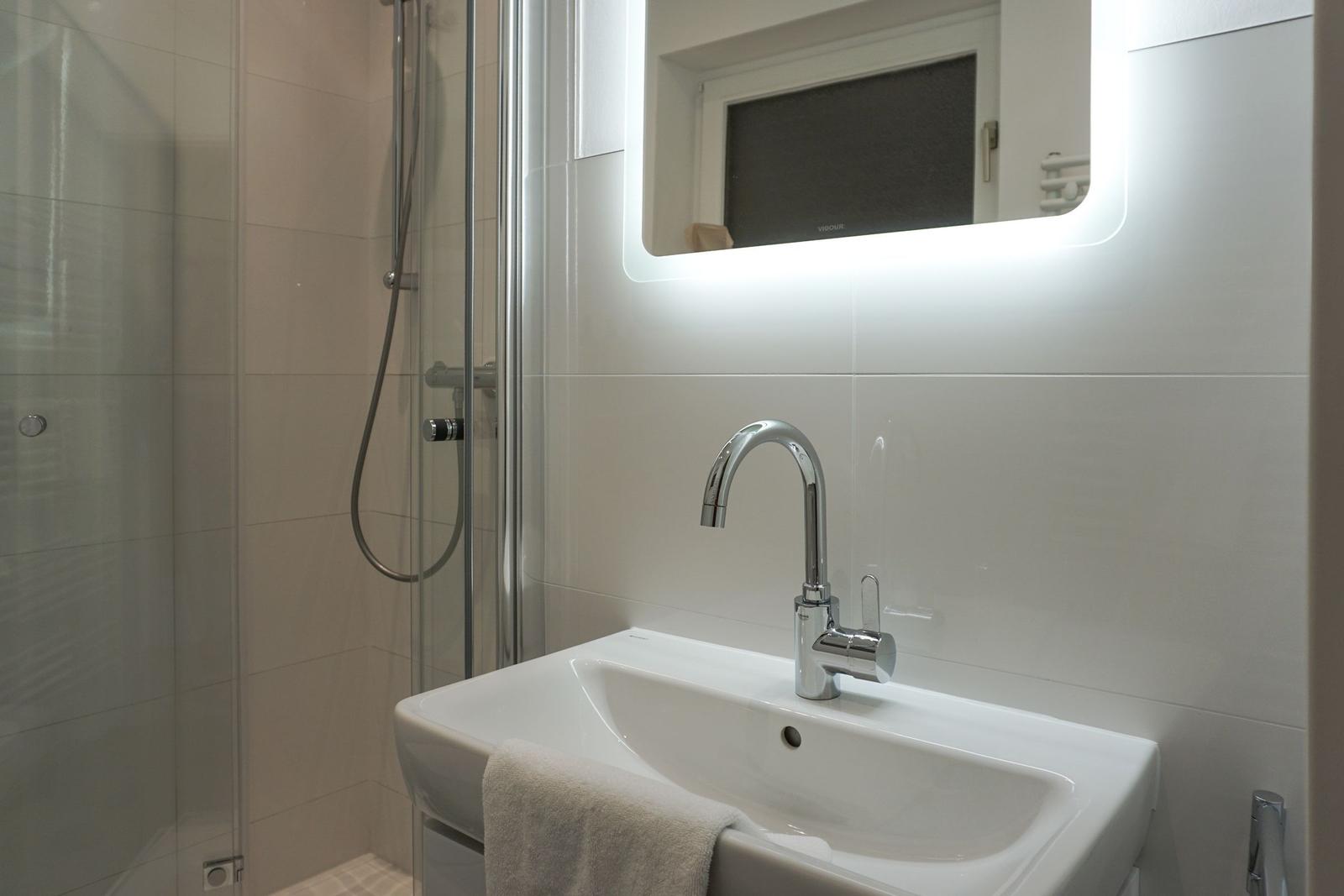 Bad mit Dusche, Waschbecken und beleuchtetem Spiegel.