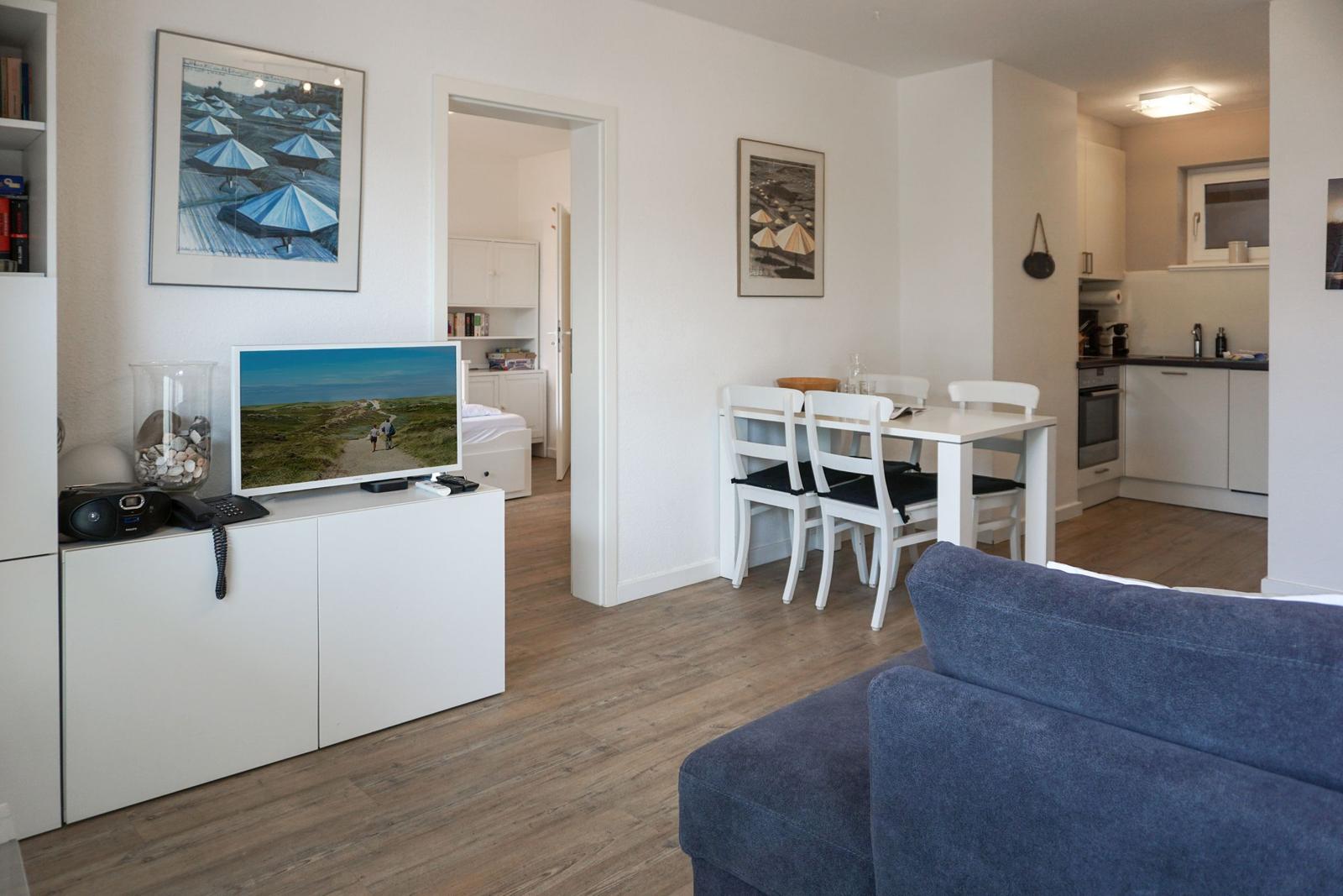 Wohn- und Essbereich mit Küchenbereich, blauer Sofa und Fernseher auf weißem Schrank.