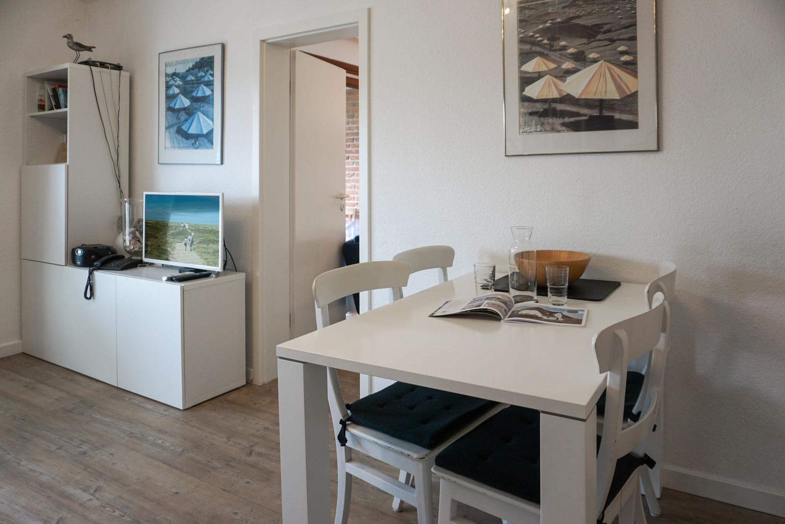 Essbereich mit weißem Tisch und Stühlen. Fernseher und Bilder an der Wand.
