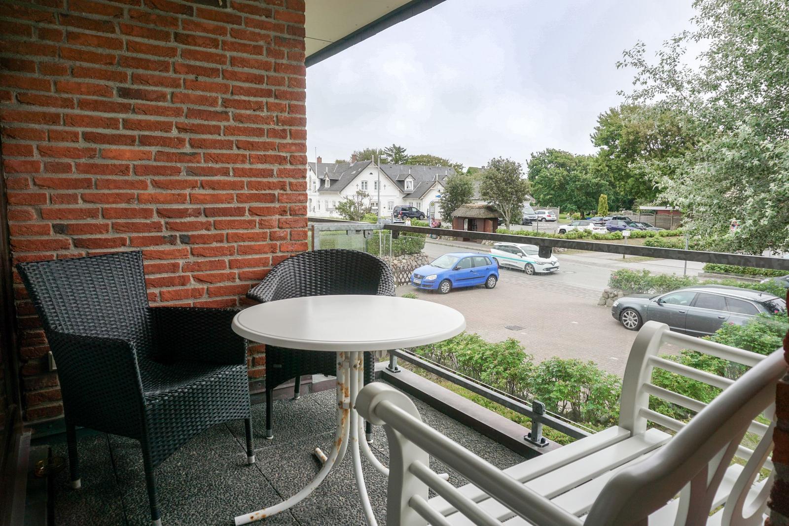 Terrasse mit Tisch und Stühlen, Blick auf Straße und Grünflächen.