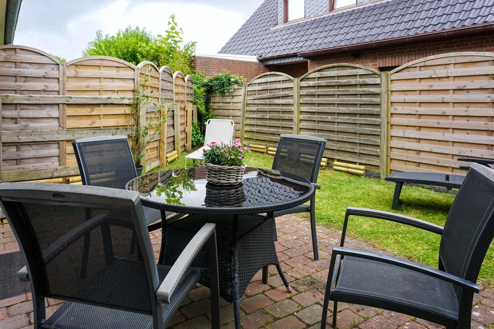 Garten mit Tisch und Stühlen, umgeben von Holzzaun und Grasfläche.
