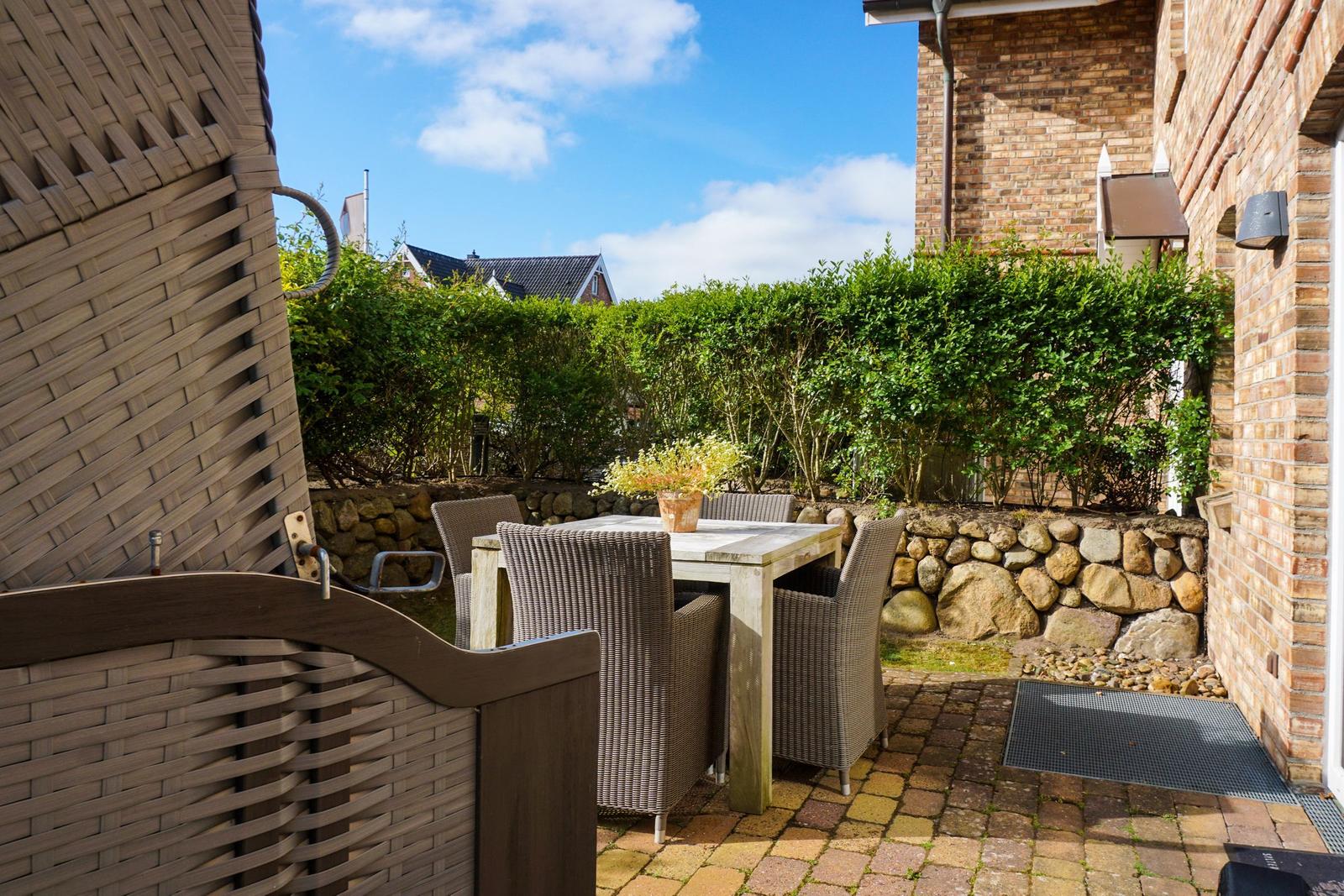 Terrace with table and chairs, surrounded by hedge and stone wall.