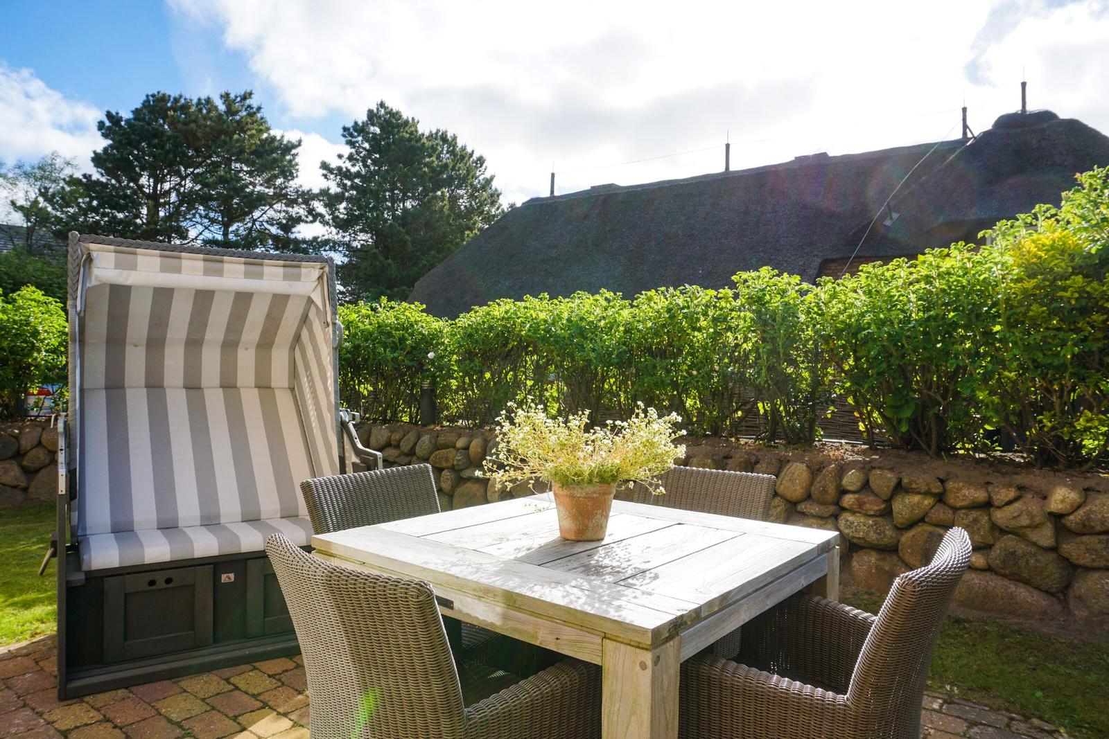 Terrace with table, chairs, and lounge. Backyard with stone wall and hedge.