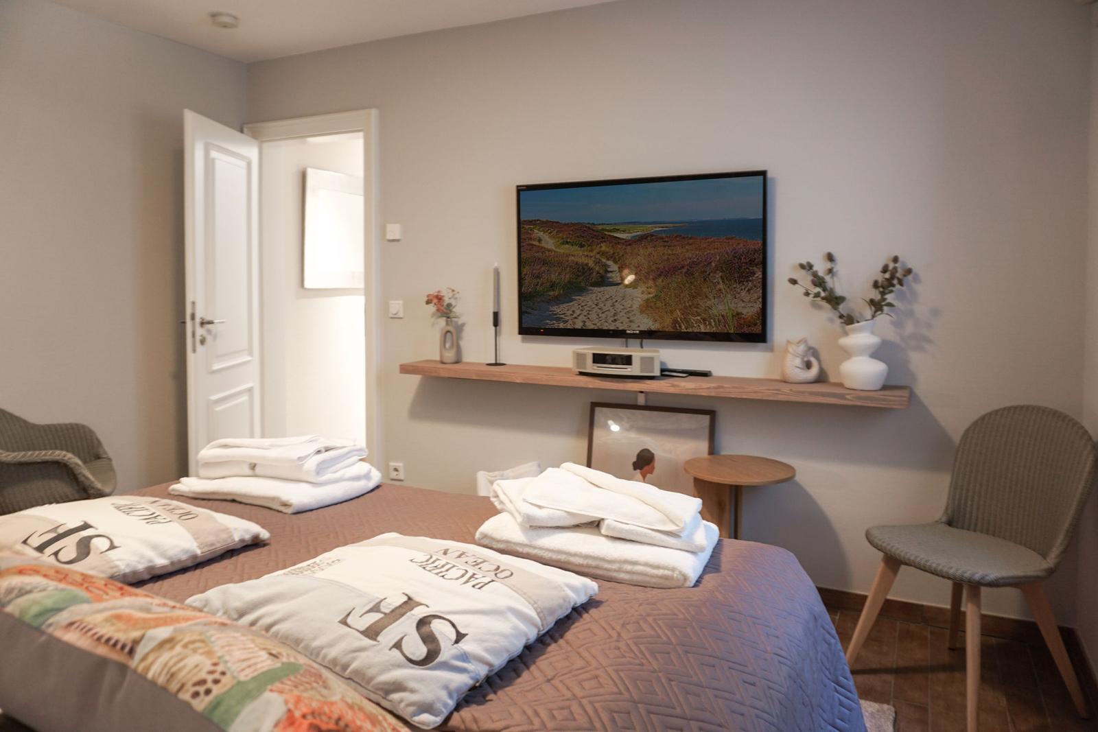 Bedroom with bed, TV, and chair. Towels are on the bed.