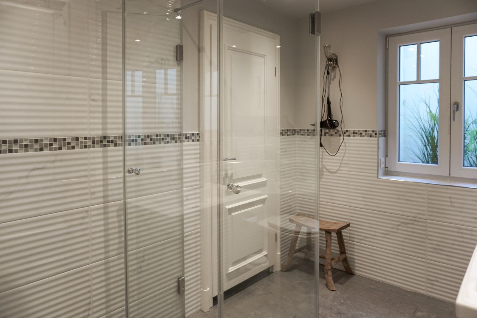Shower cabin with glass wall, wooden stool, and window with view of plants.