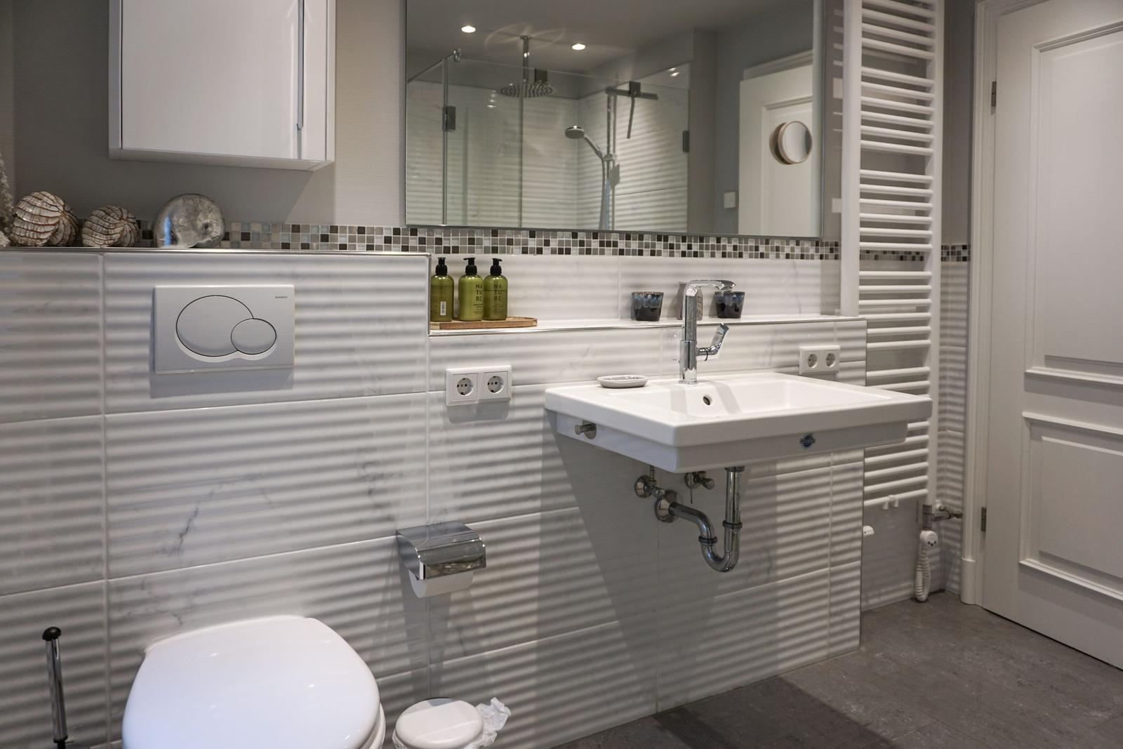 Bathroom with toilet, sink, and shower. Wall cladding with mosaic and shell.