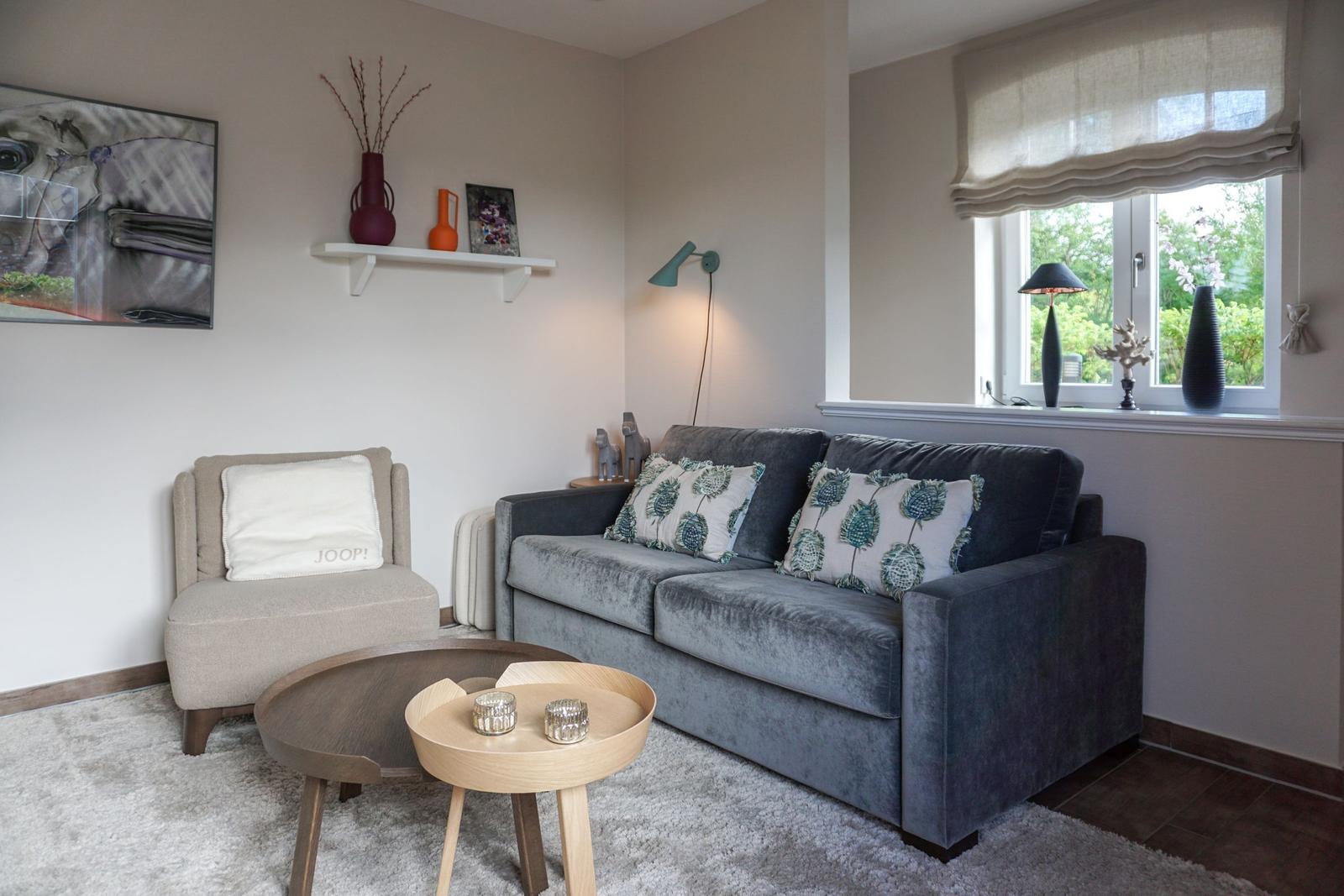 Living room with gray sofa, armchair, and round tables. Window with view of greenery.