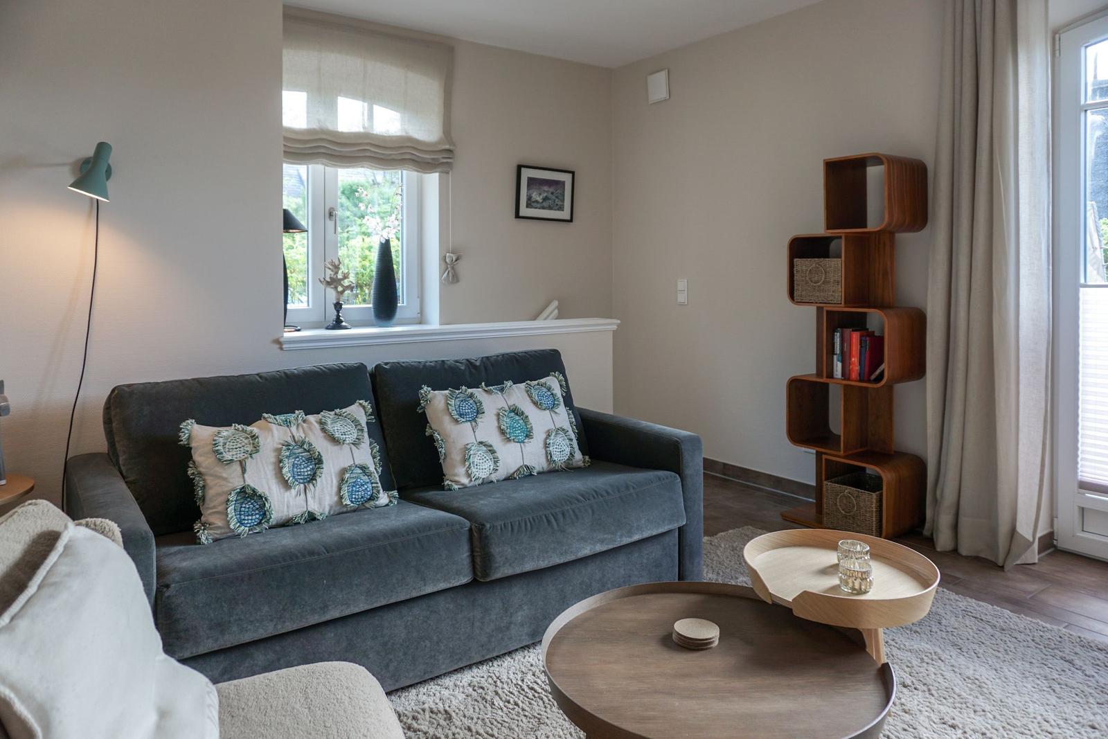 A living room with a gray sofa, round table, and wooden shelf.
