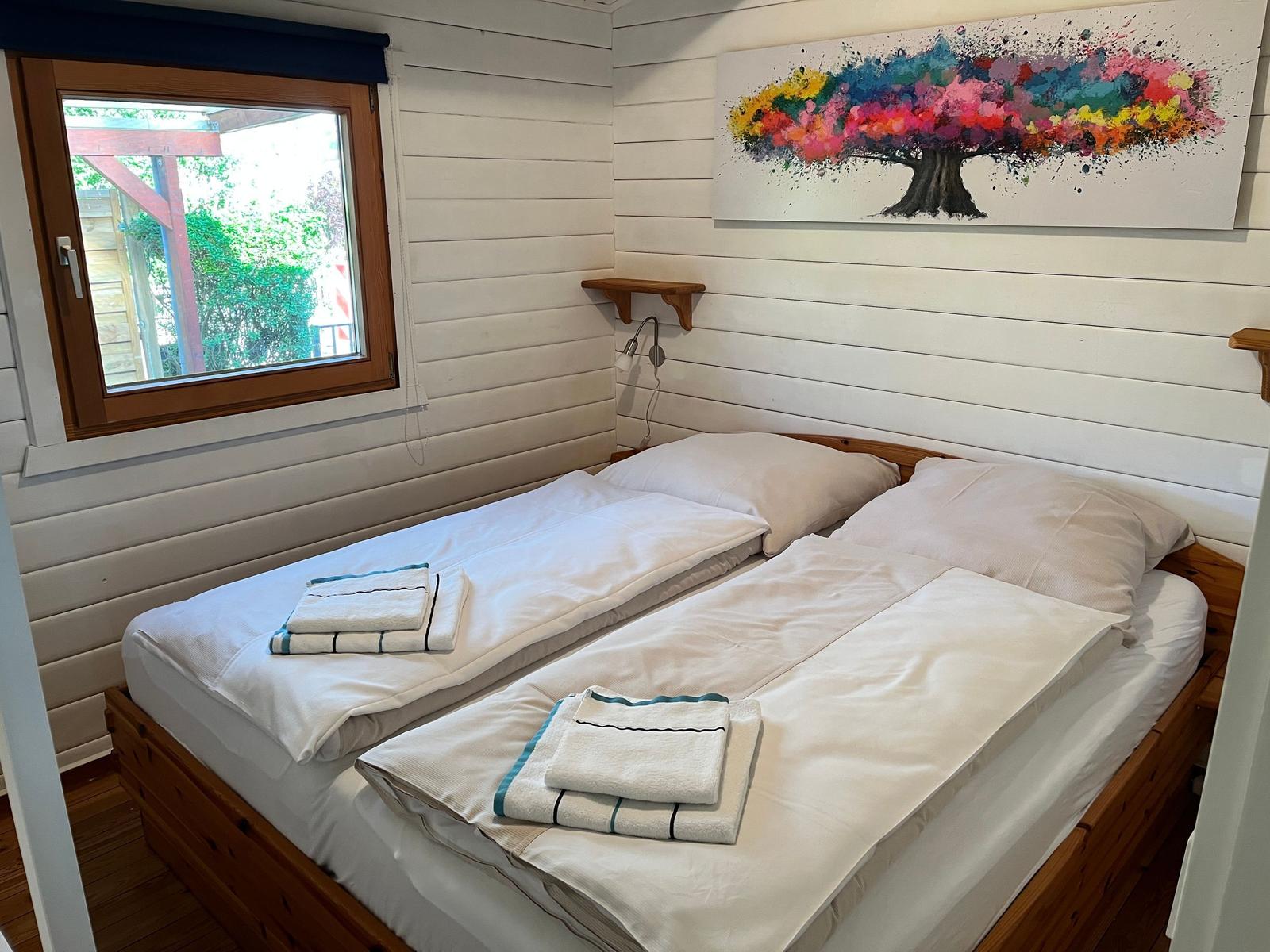Zwei Betten mit weißen Laken und Handtüchern. Wandbild und Fenster mit Blick nach draußen.