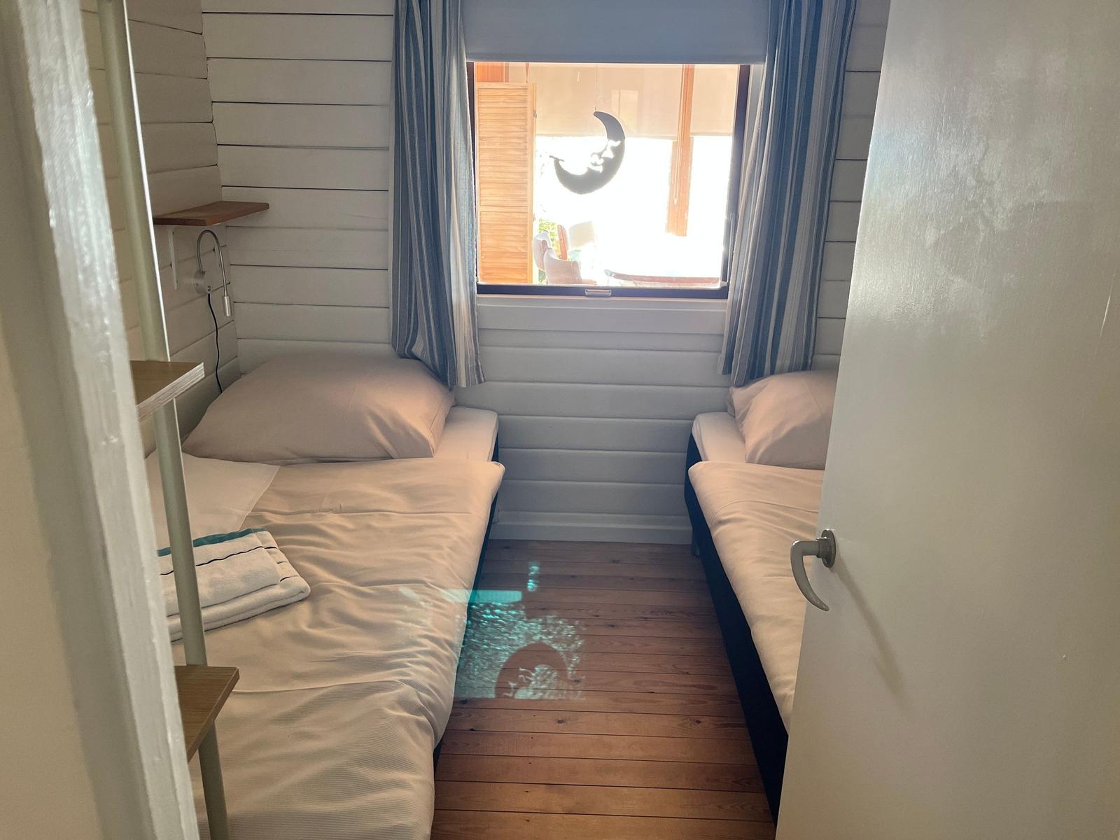 Zwei Betten in einem Raum mit Holzboden und Fenster mit Vorhängen.
