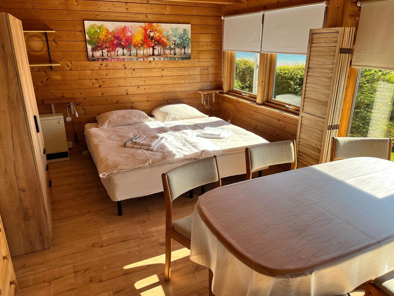 Schlafzimmer mit Doppelbett, Tisch und Stühlen, Holzwand und Fenster mit Blick.