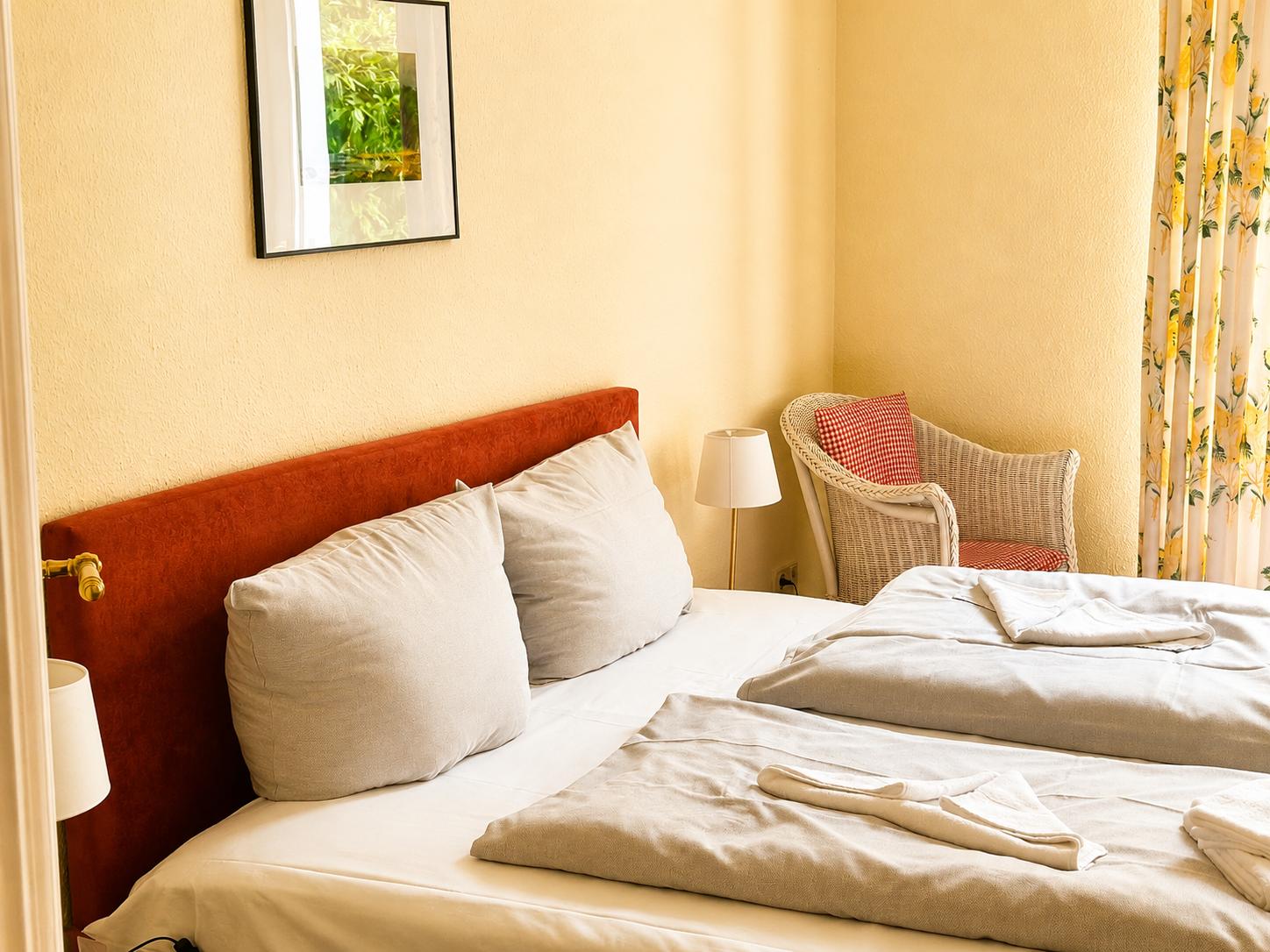 Ein Schlafzimmer mit Doppelbett, rotem Kopfteil, Stuhl und Vorhang mit Blumenmuster.