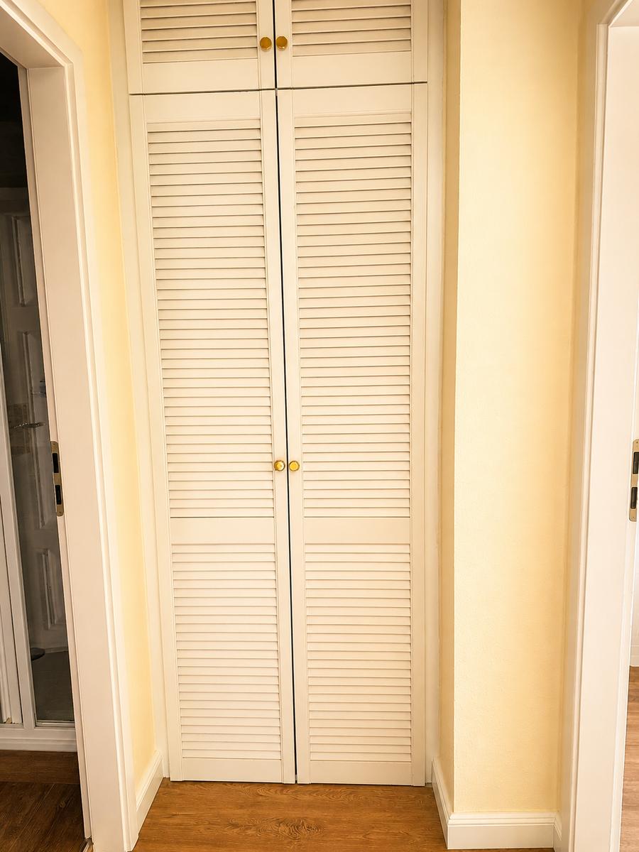Schwebetüren-Kleiderschrank mit goldenen Knöpfen und Holzboden.