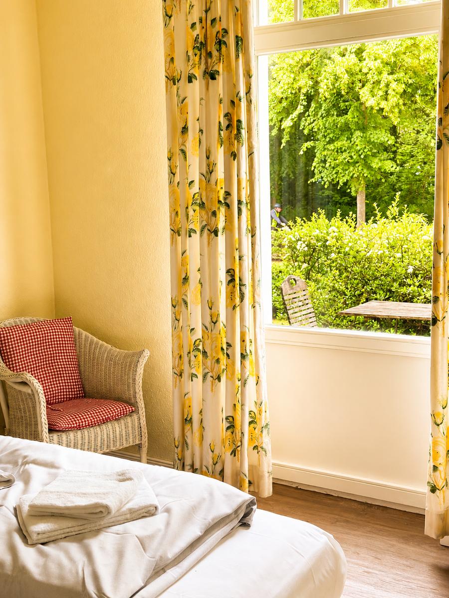 Ein Zimmer mit Bett, Stuhl und Blick auf einen Garten.