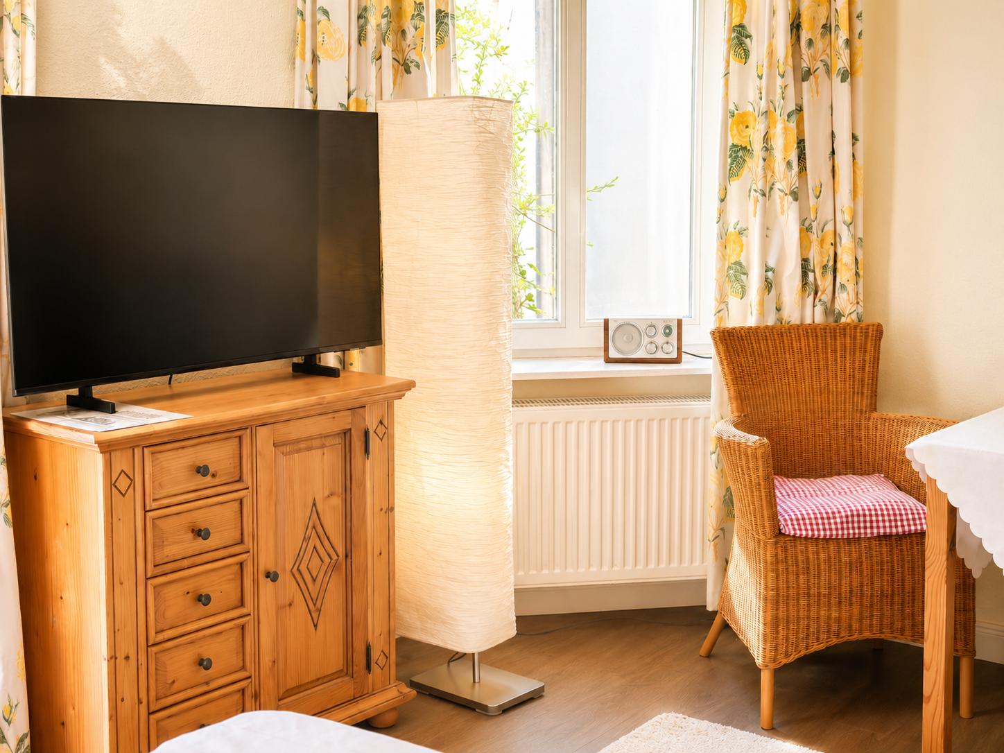 Ein Raum mit Fernseher, Wickerstuhl und Fenster mit Vorhängen.