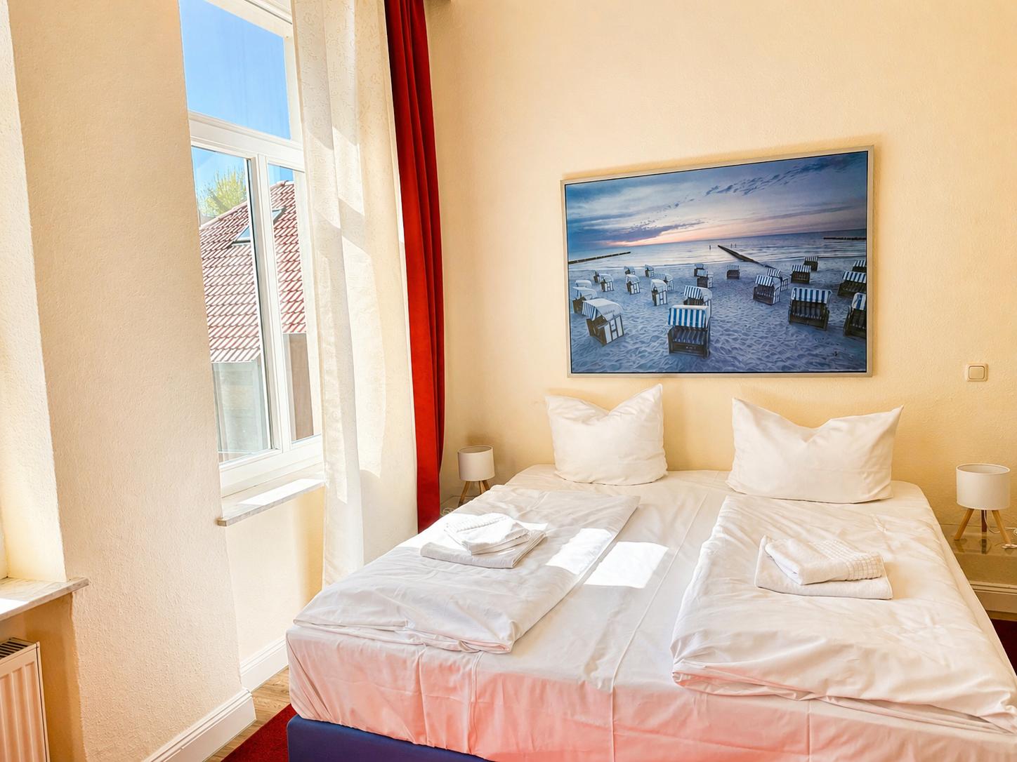 Schlafzimmer mit Doppelbett, Fenster und Strandbild an der Wand.