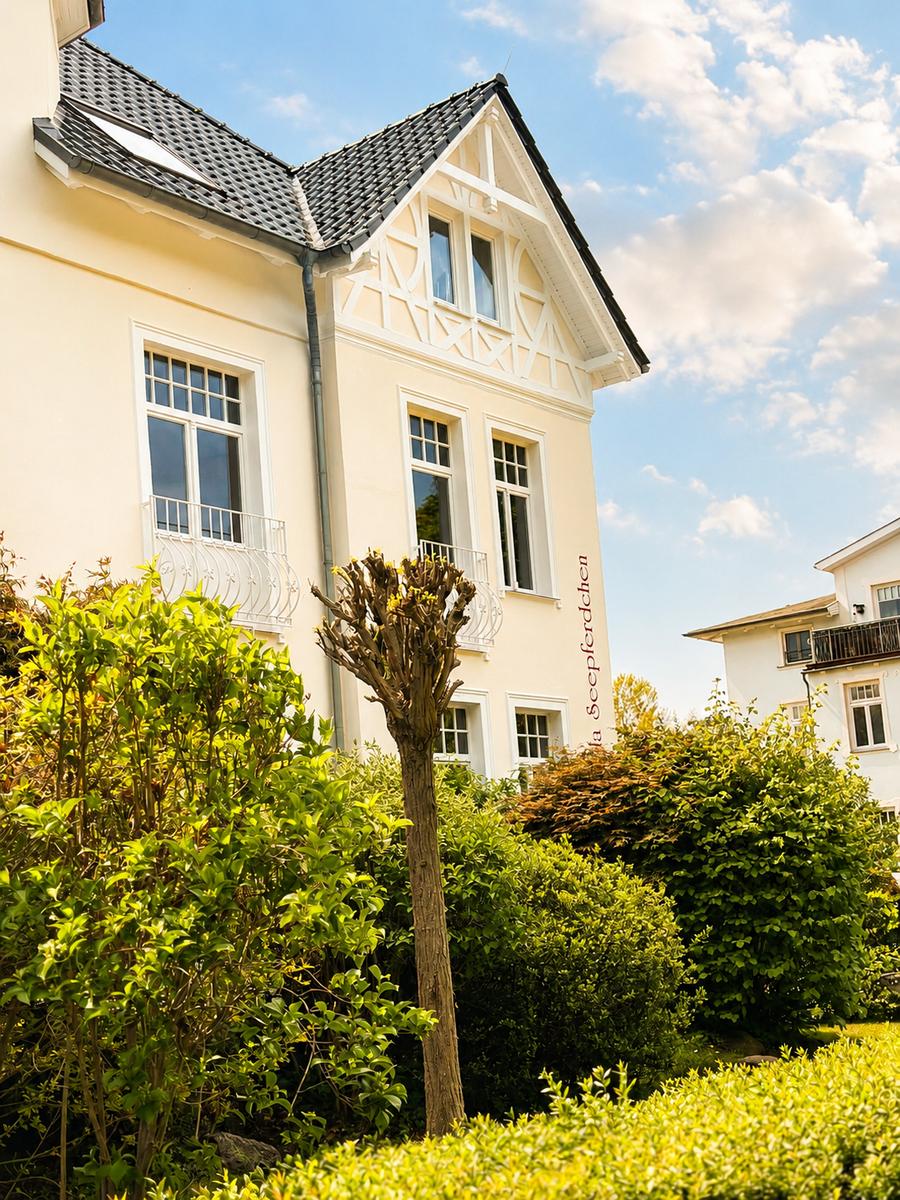 Haus mit Balkonen und grüner Umgebung unter blauem Himmel.