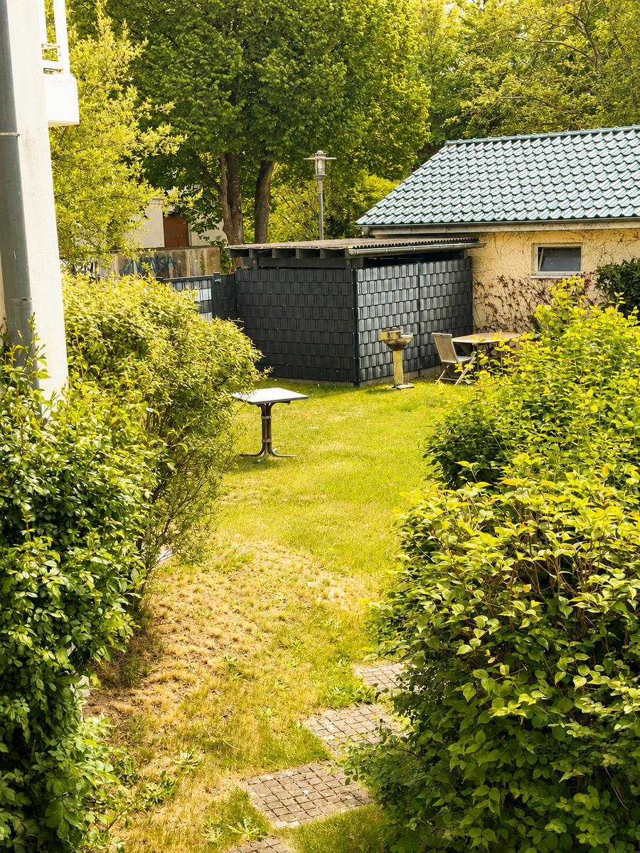 Hinterhof mit Grünfläche, Tisch, Gartenhaus und Bäumen