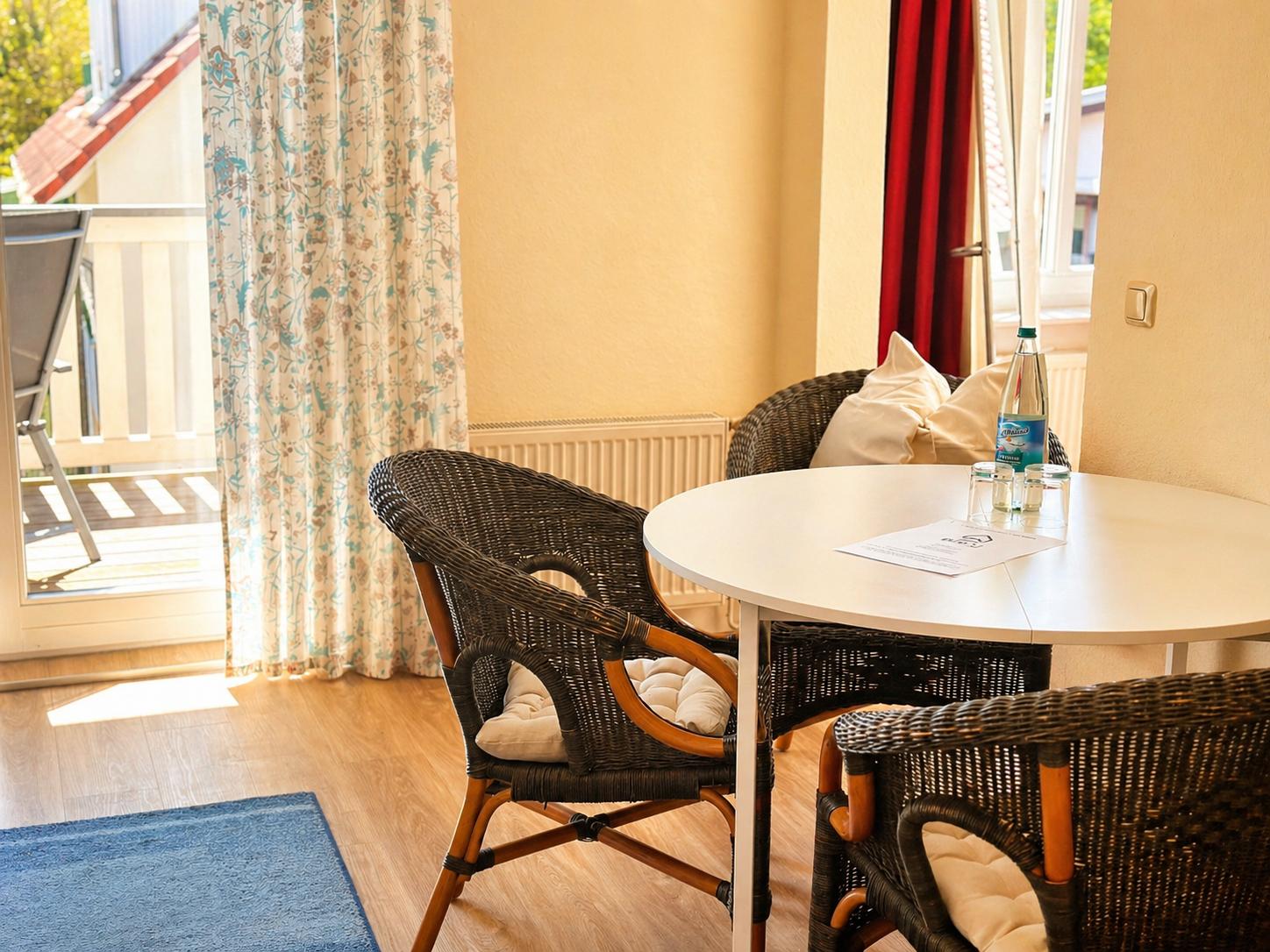 Rundtisch mit drei Stühlen, Fliesenboden, Vorhang und Balkon.