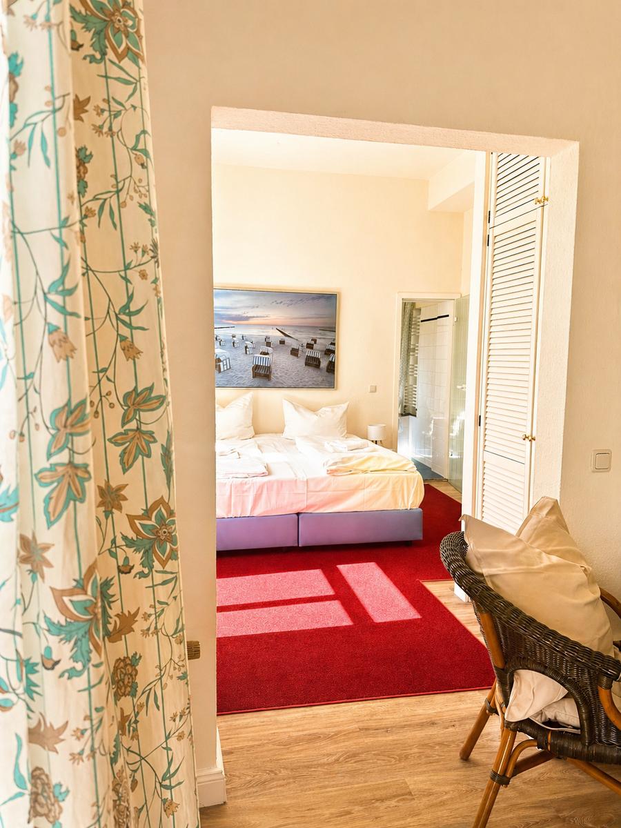 Schlafzimmer mit Bett, rotem Teppich und Wandbild. Blick auf Badezimmer.