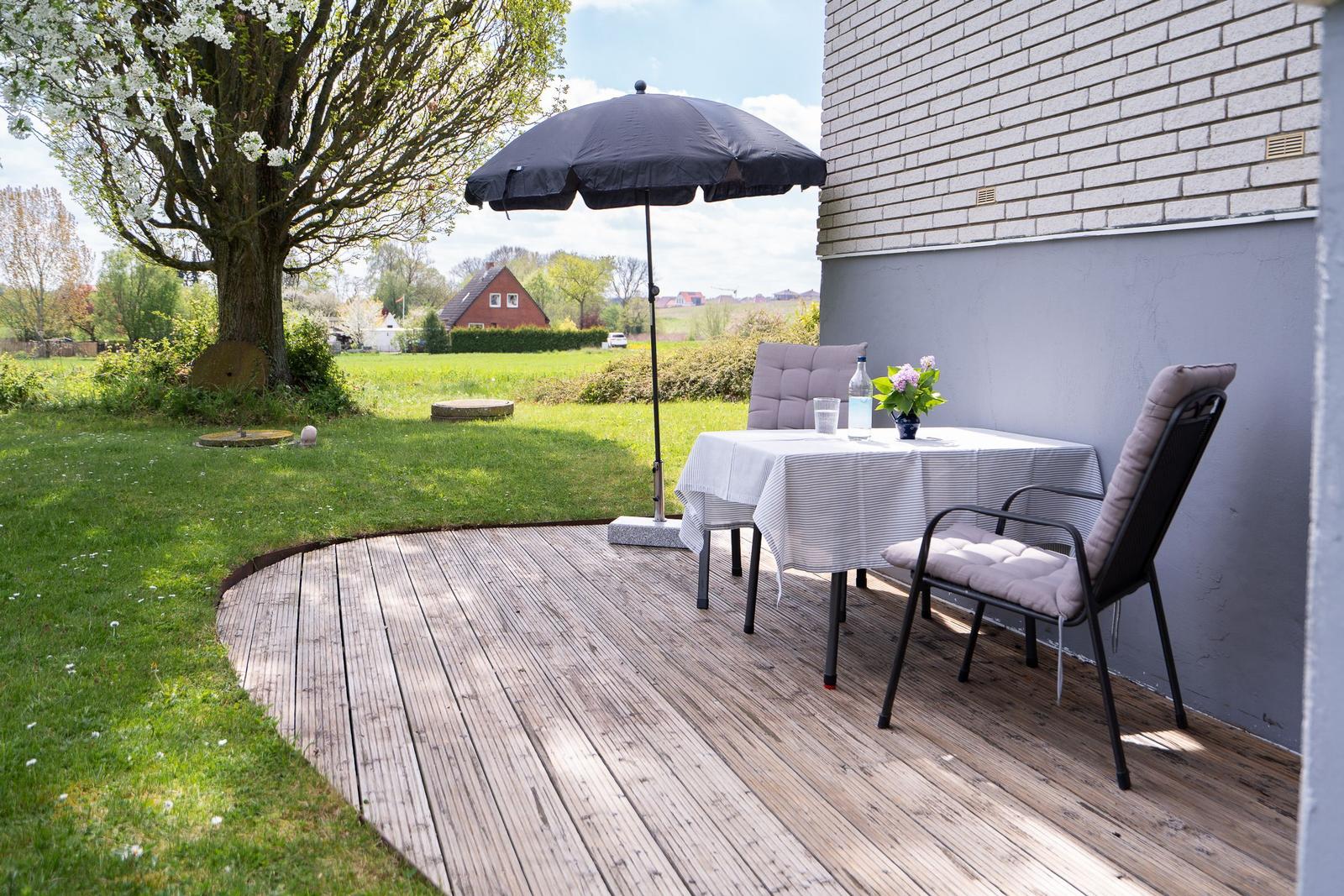 Terrace with table, chairs, and umbrella next to house wall